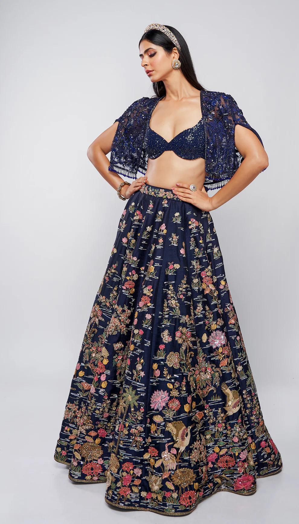Model wearing a dark blue floral lehenga on a runway with a blurred floral background for designers Shyamal and Bhumika