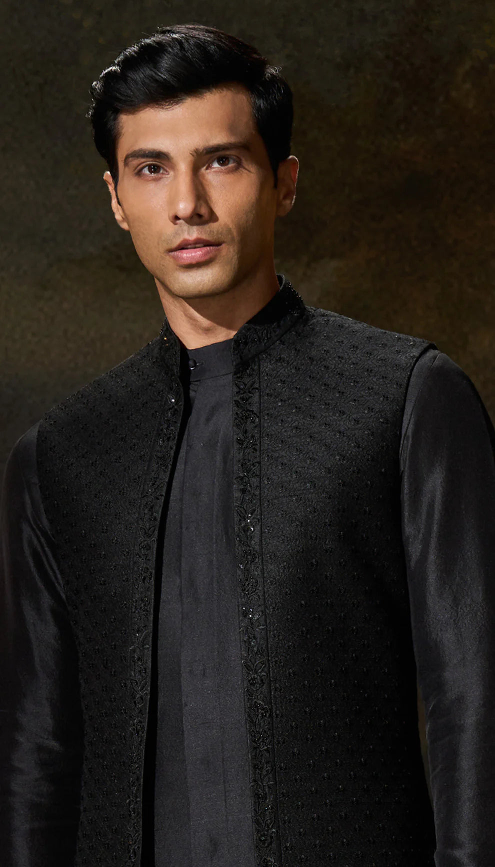 Man wearing a black open jacket by designers Shyamal and Bhumika, standing in an elegant room with decorative elements.