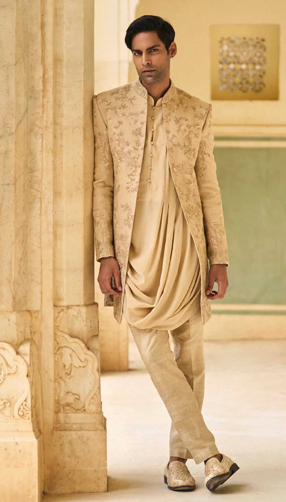 Man wearing a traditional beige open jacket by designers Shyamal and Bhumika, in an elegant interior setting