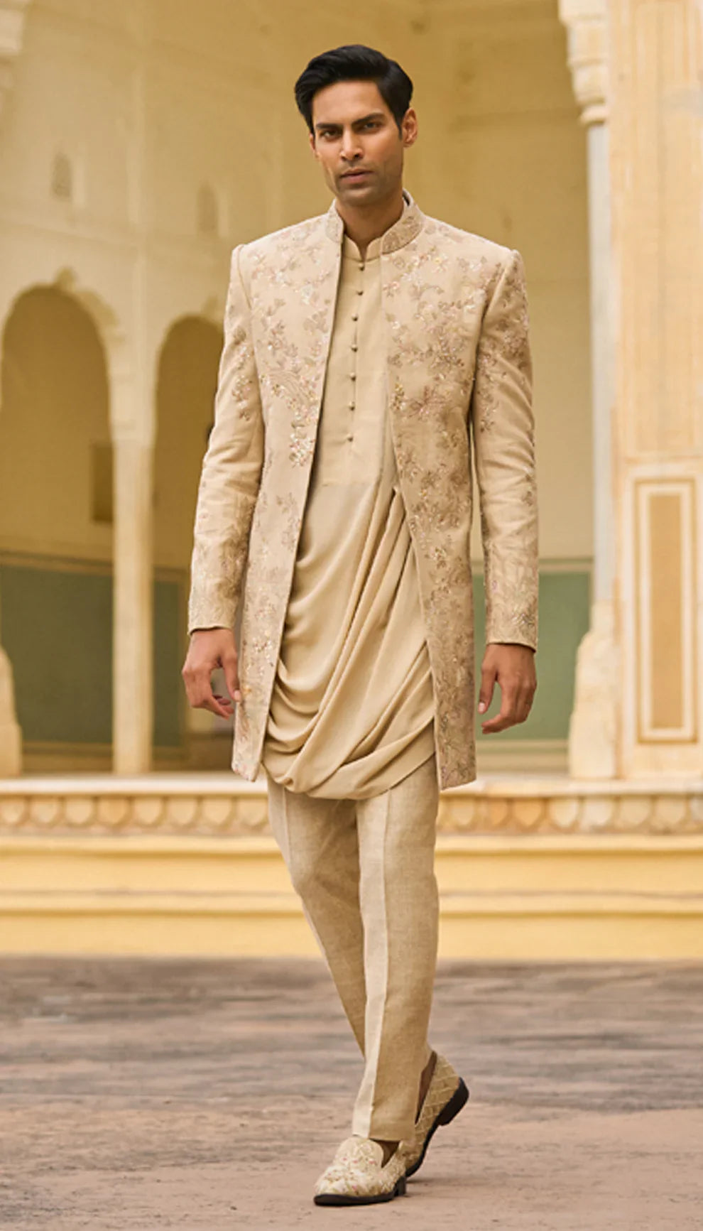 Man wearing a traditional beige open jacket by designers Shyamal and Bhumika, in an elegant interior setting
