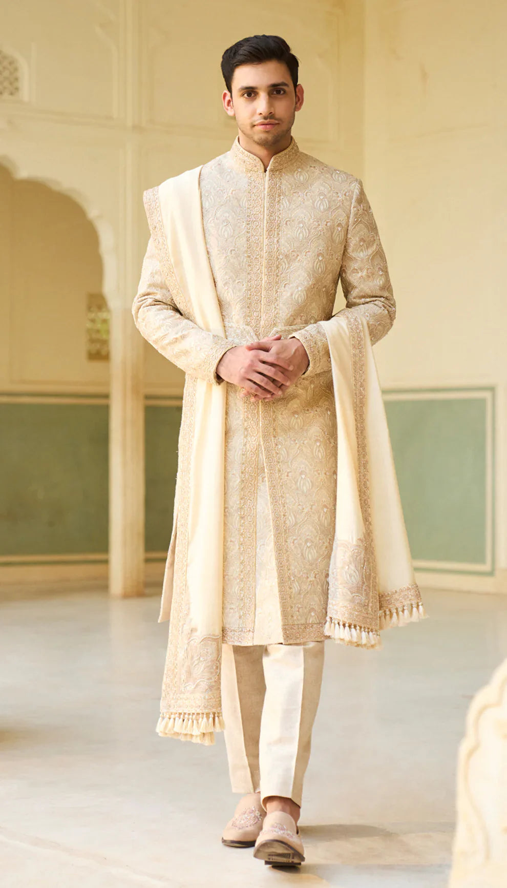 Man wearing a beige sherwani by designers Shyamal and Bhumika, in an elegant indoor setting