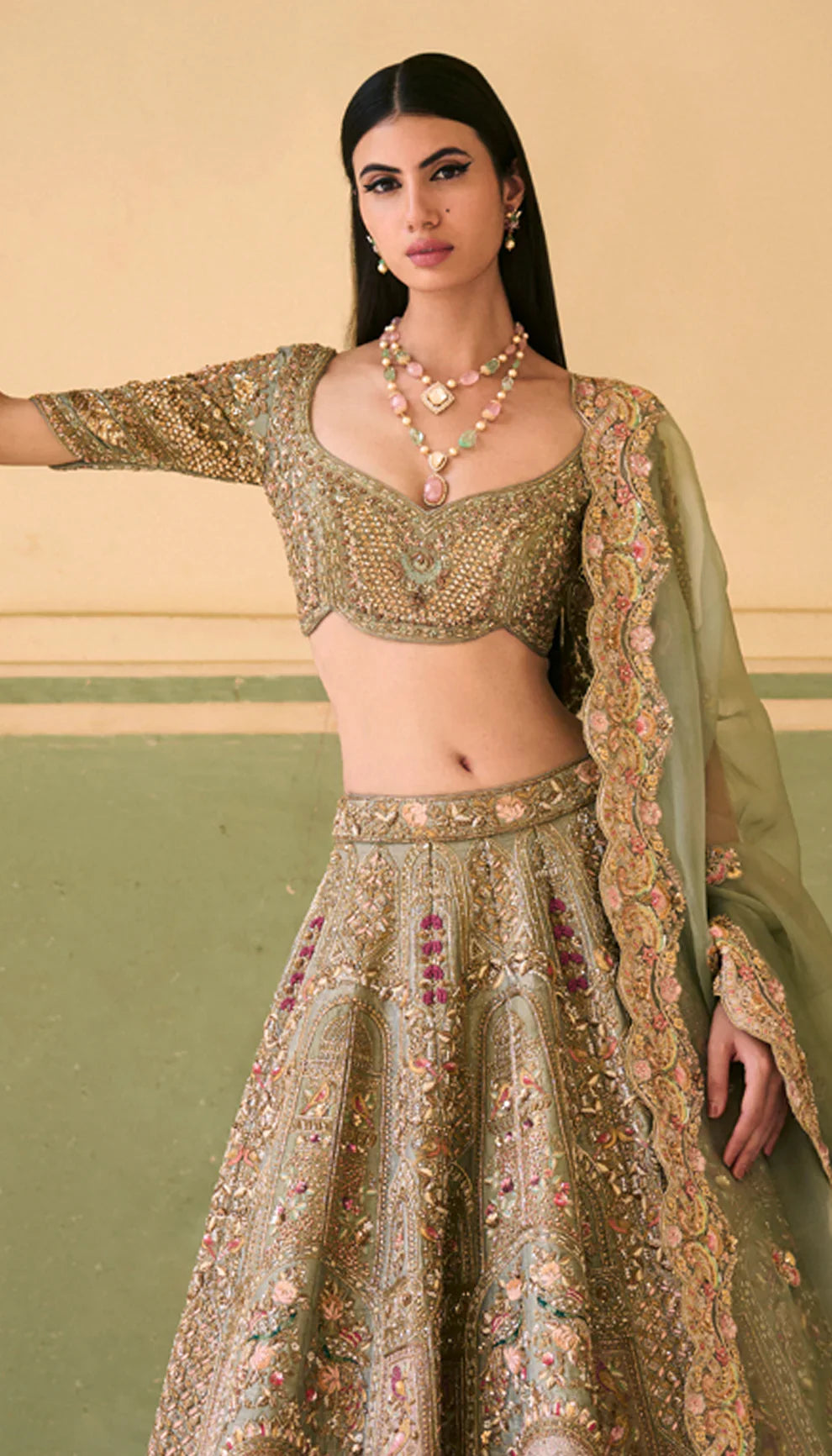 Woman in a sage green traditional embroidered lehenga with a green dupatta against a neutral background