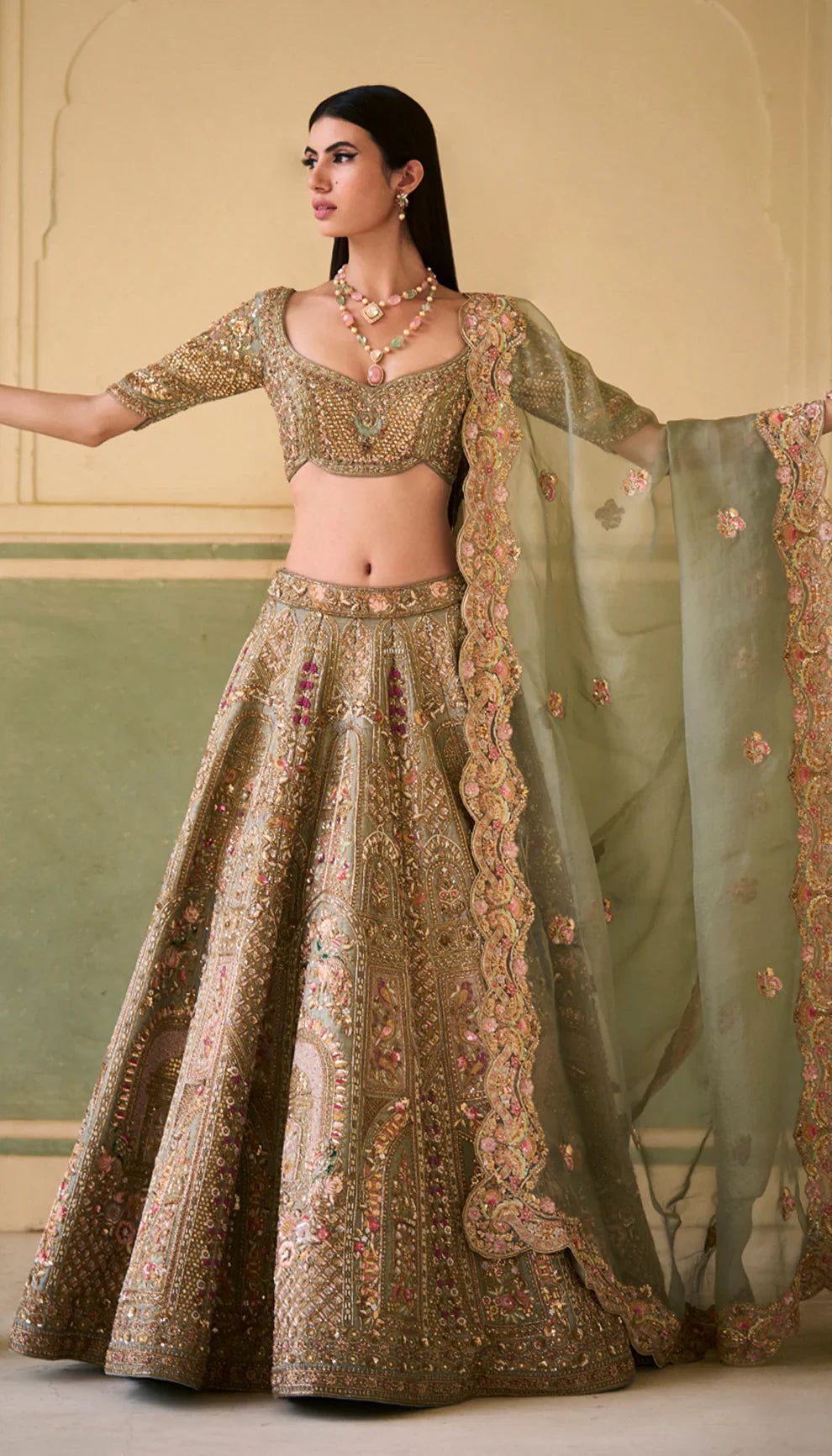 Woman in a sage green traditional embroidered lehenga with a green dupatta against a neutral background