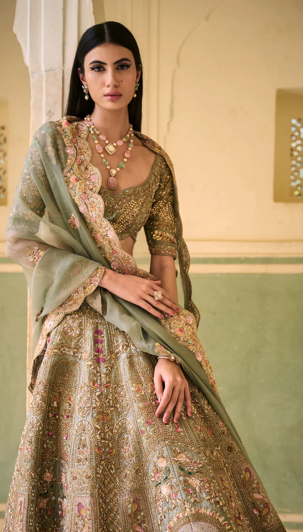 Woman in a sage green traditional embroidered lehenga with a green dupatta against a neutral background