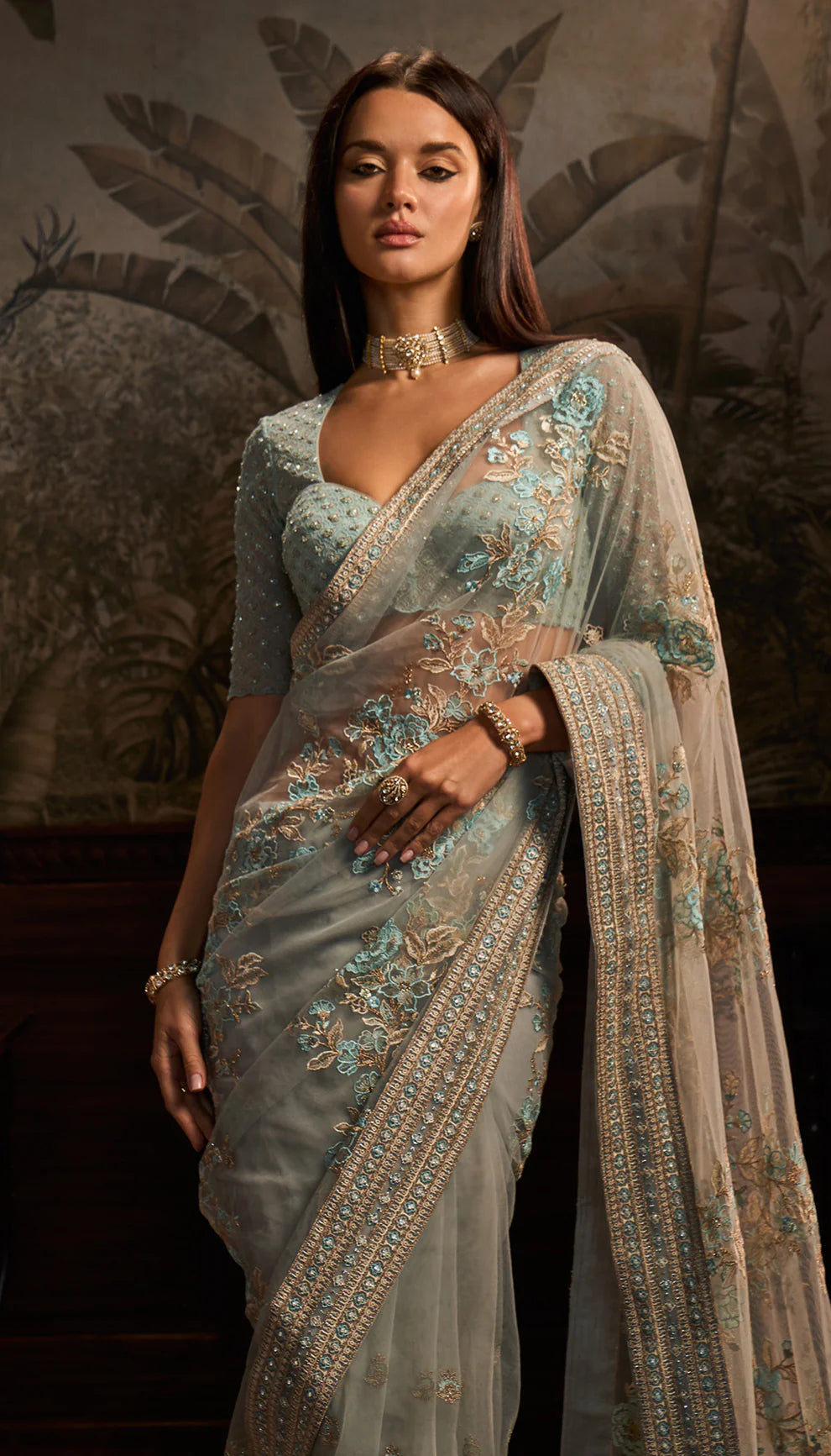 Woman wearing a light blue net saree with a matching blouse by designers Shyamal and Bhumika in a decorative setting.