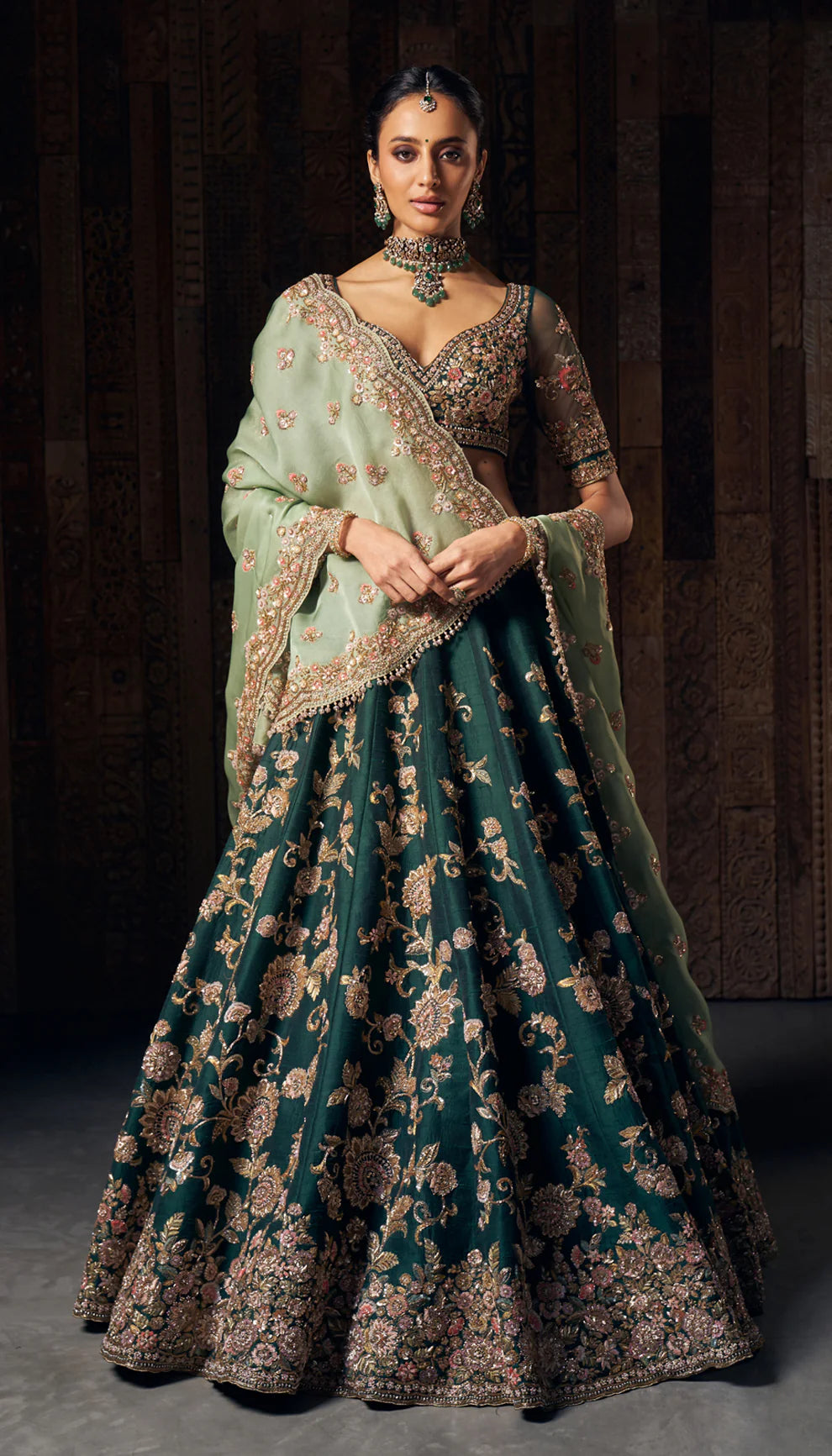 Woman wearing a traditional green and gold lehenga by designers Shyamal and Bhumika with a dark background