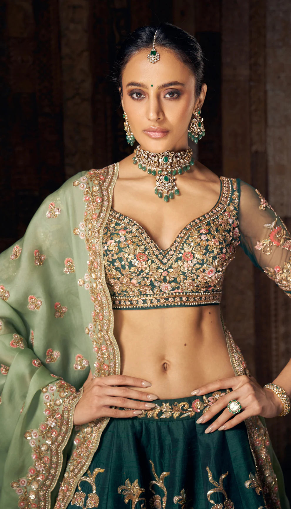 Woman wearing a traditional green and gold lehenga by designers Shyamal and Bhumika with a dark background.