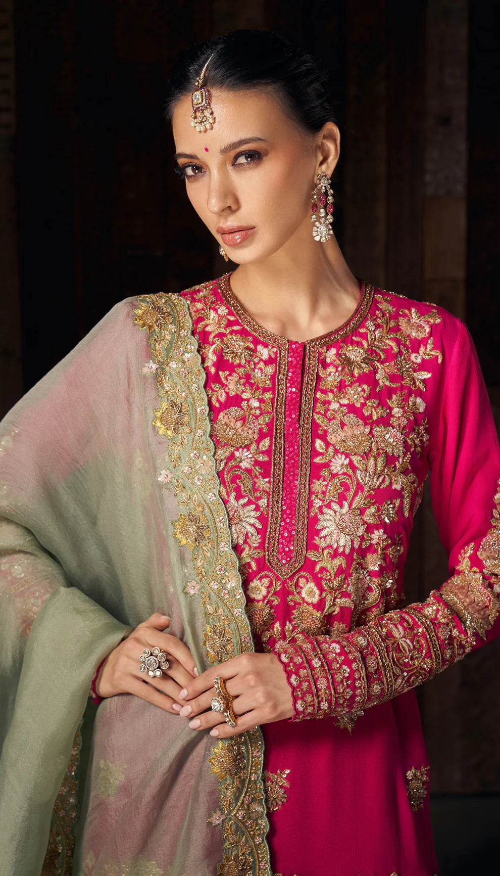 Woman wearing a pink traditional sharara set by designers Shyamal and Bhumika with gold embroidery against a dark background