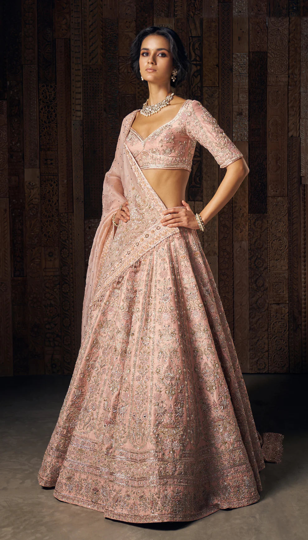 Woman wearing a traditional light pink embroidered lehenga by designers Shyamal and Bhumika against a dark background