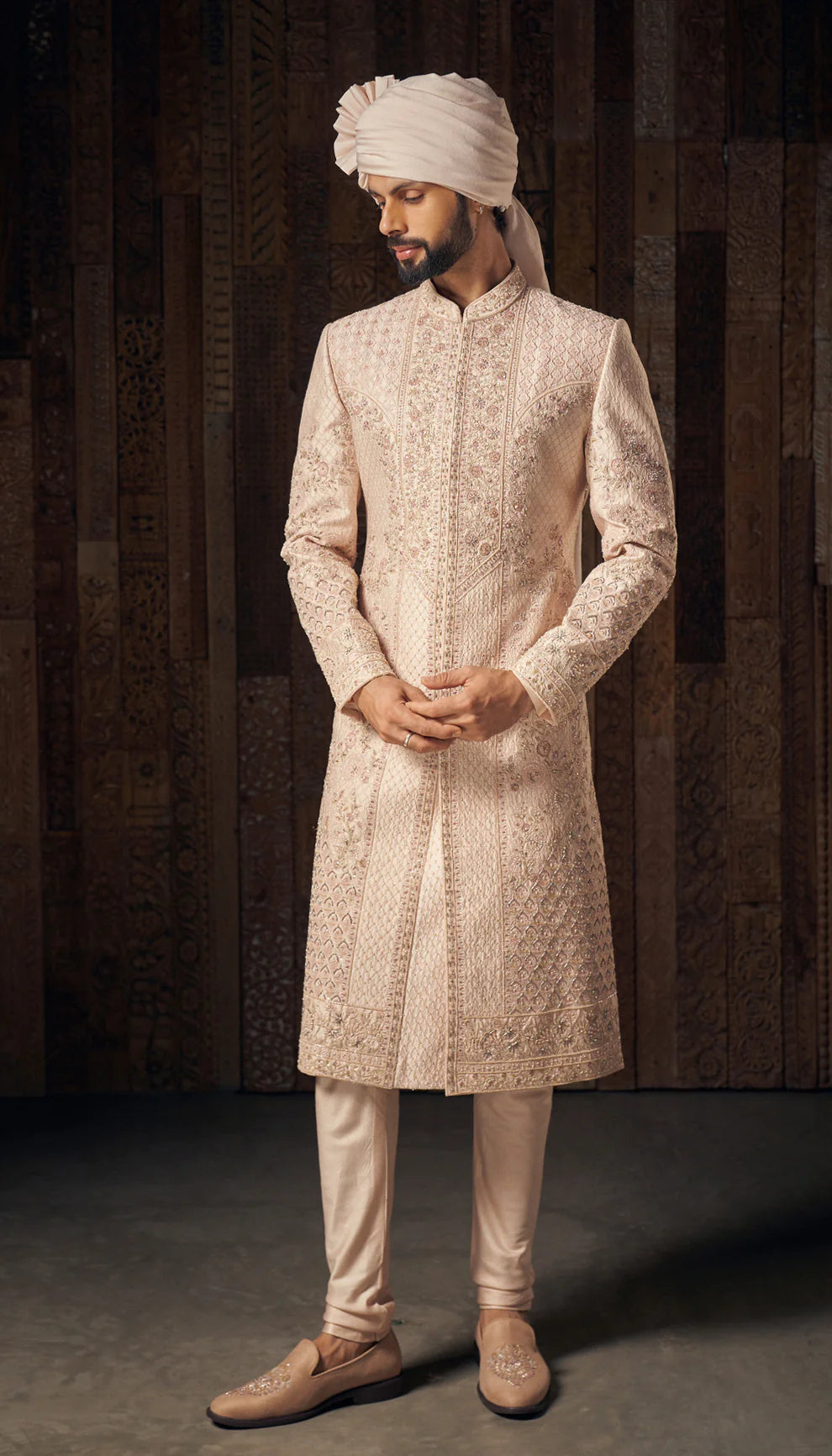 Man wearing a traditional cream sherwani with a turban by designers Shyamal and Bhumika against a dark background