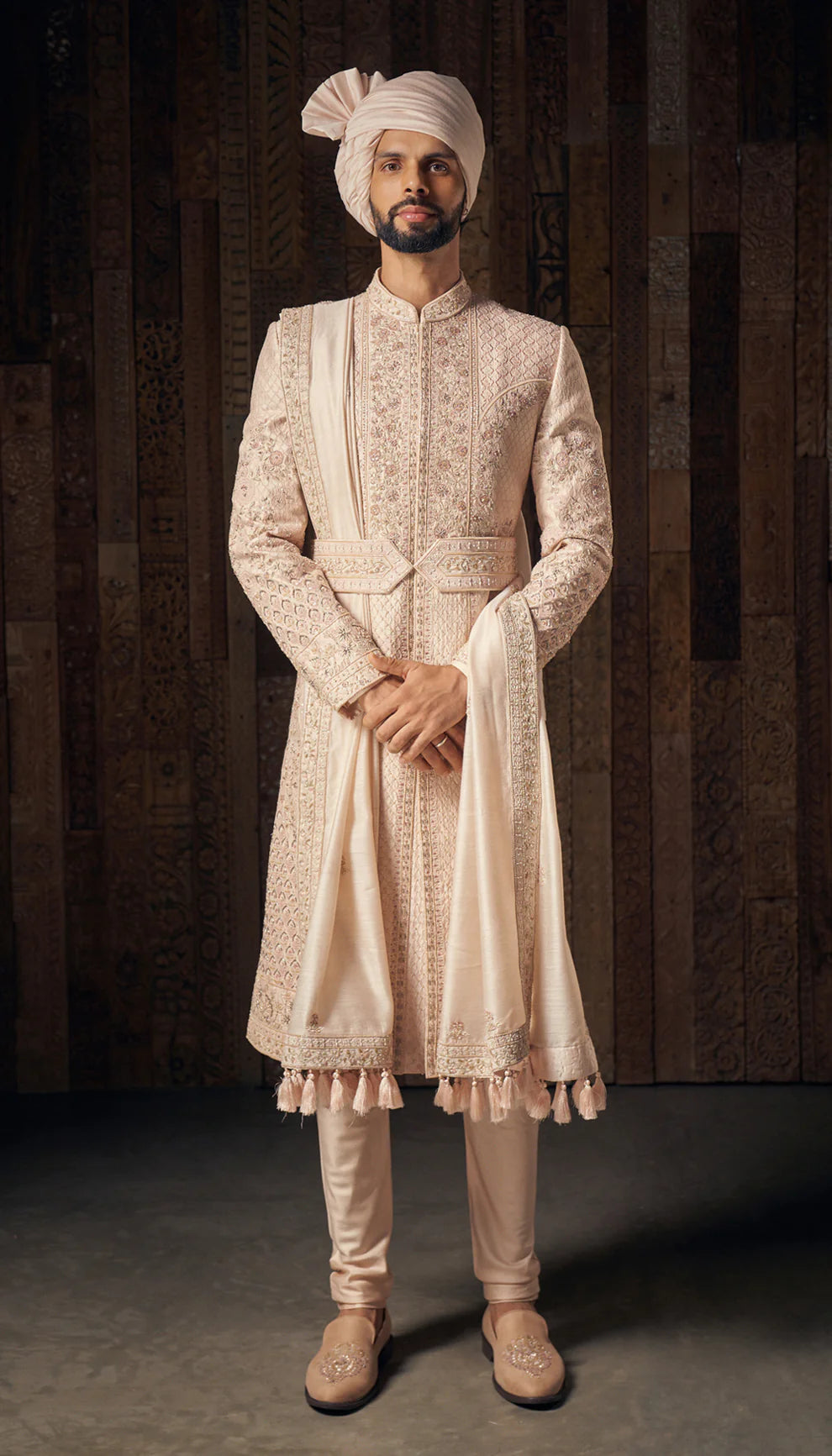 Man wearing a traditional cream sherwani with a turban by designers Shyamal and Bhumika against a dark background