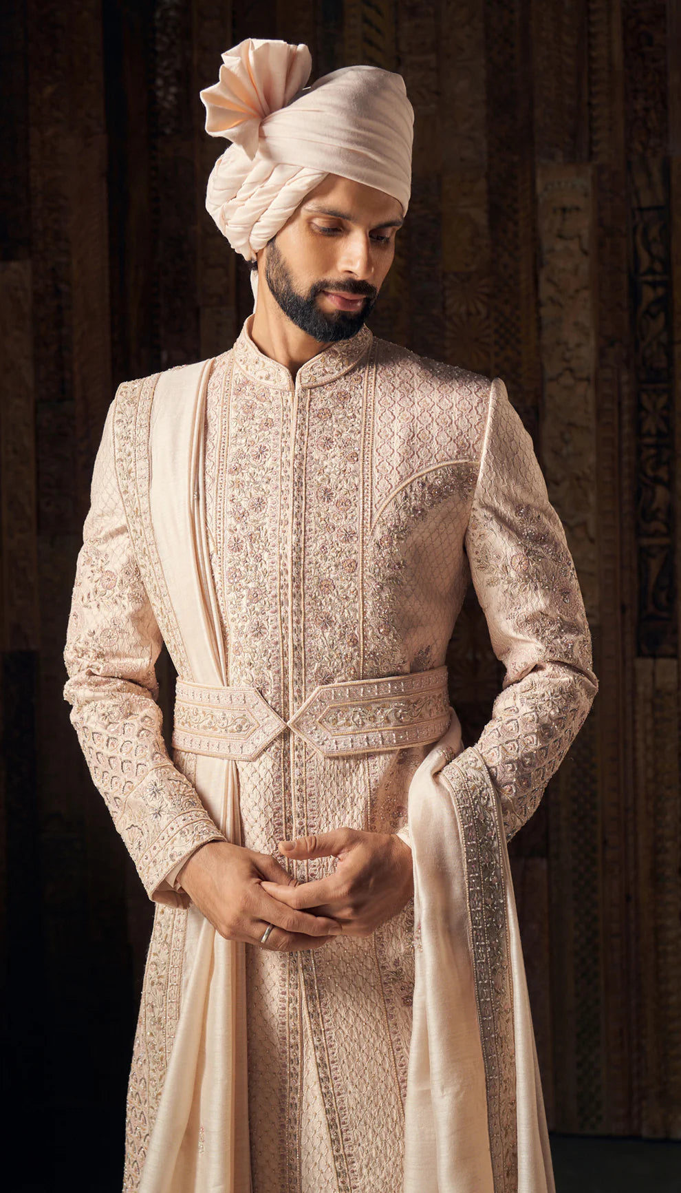 Man wearing a traditional cream sherwani with a turban by designers Shyamal and Bhumika against a dark background