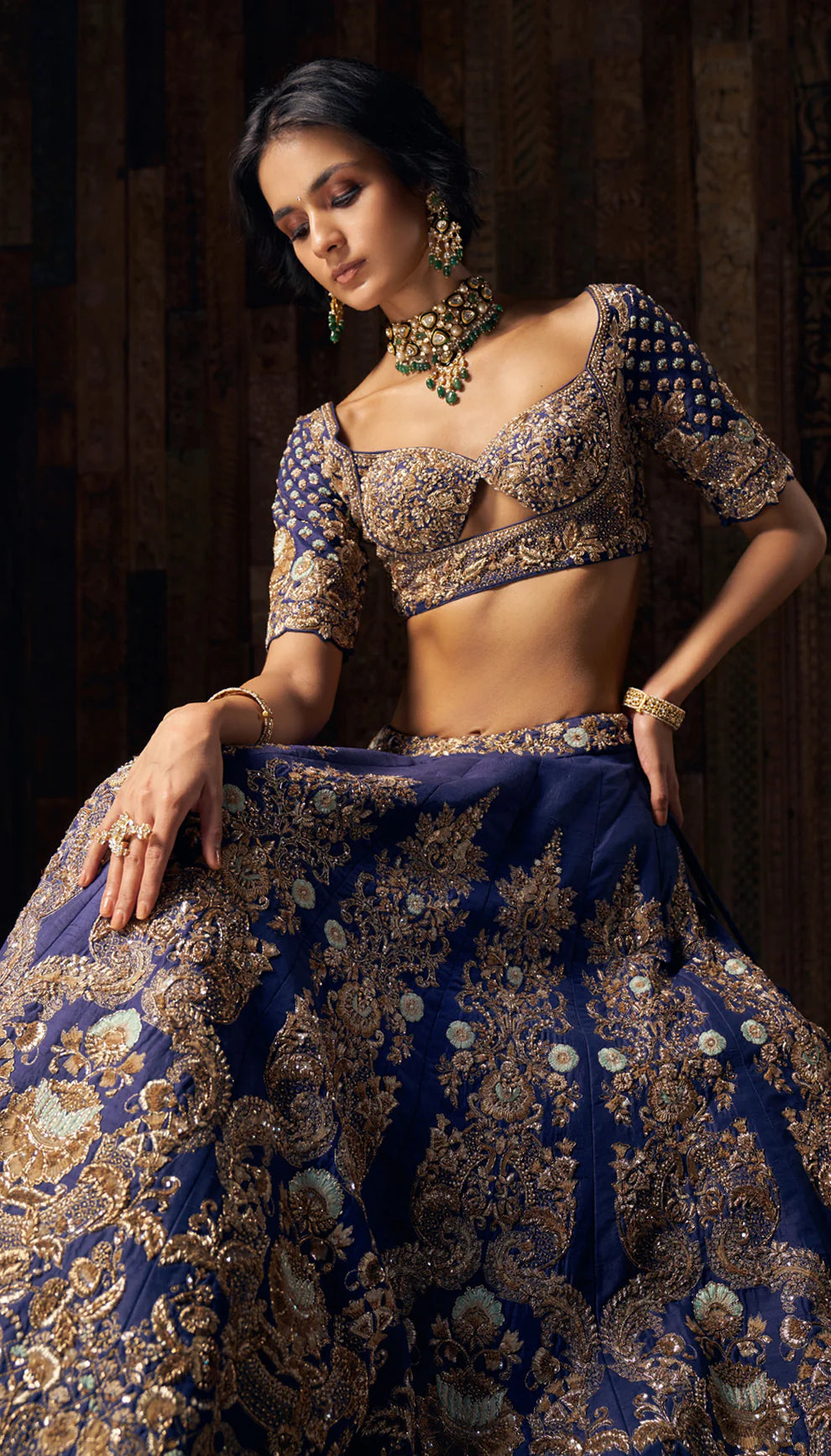 Woman in a blue gold embroidered lehenga by designers Shyamal and Bhumika against a dark backdrop.