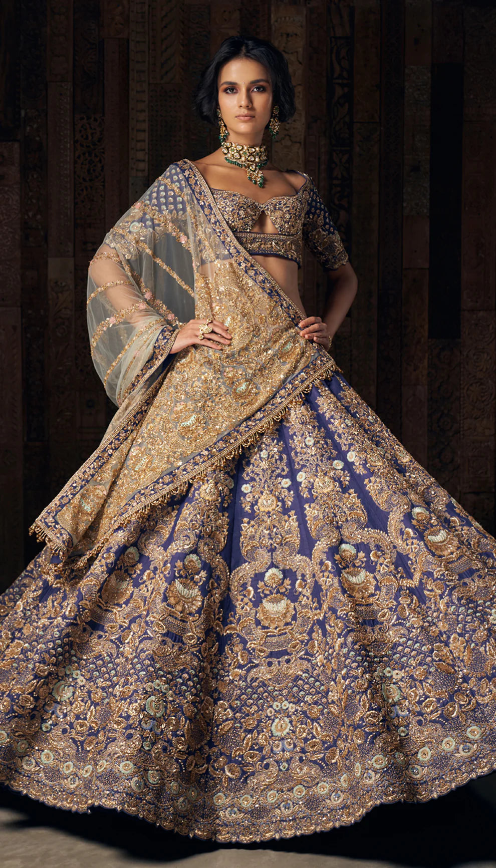 Woman in a blue gold embroidered lehenga by designers Shyamal and Bhumika against a dark backdrop.