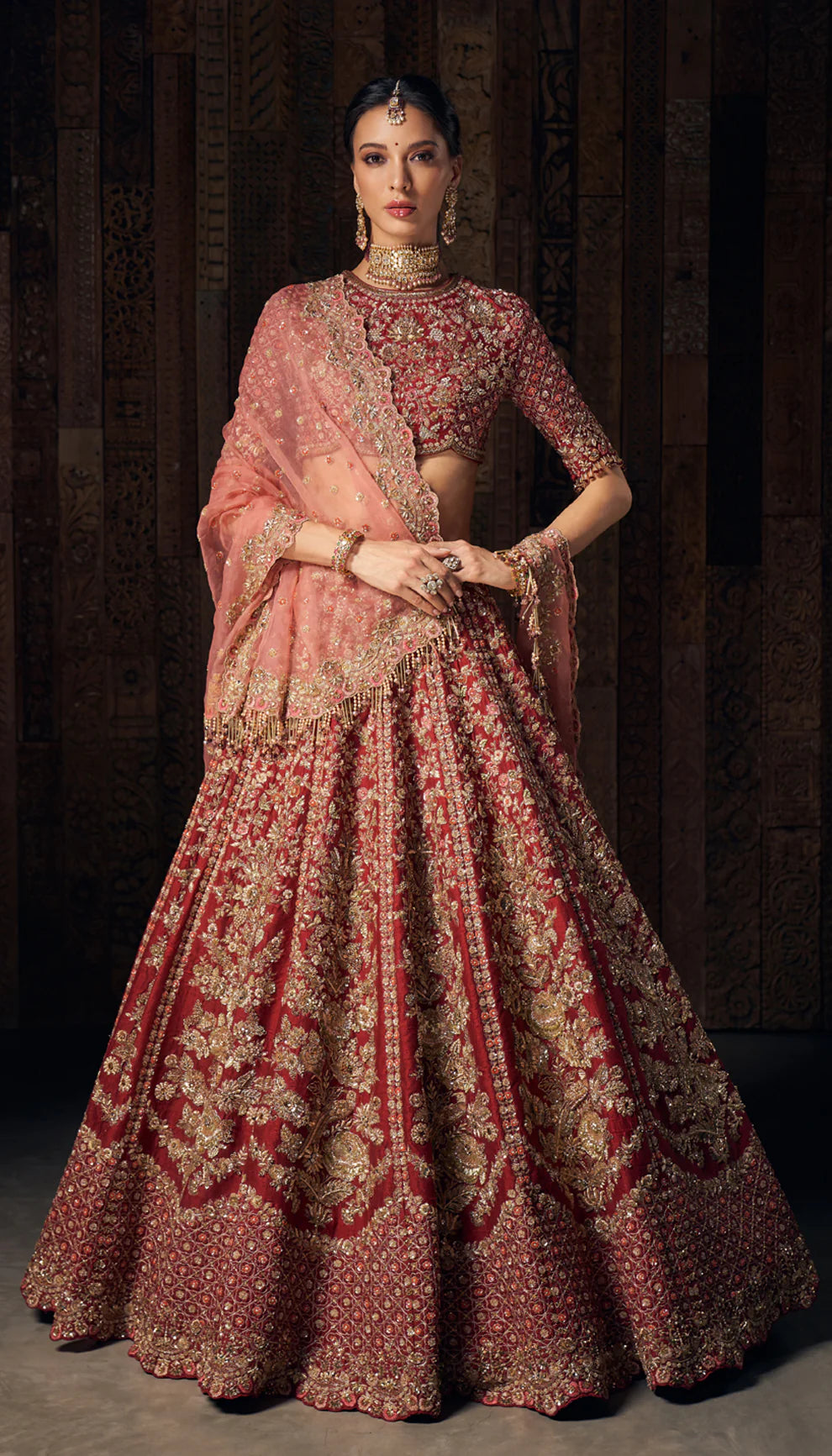 Woman in deep red gold embroidered bridal lehenga by designers Shyamal and Bhumika, against a dark backdrop