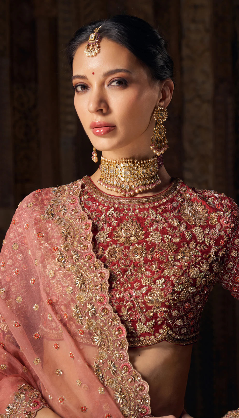 Woman in deep red gold embroidered bridal lehenga by designers Shyamal and Bhumika, against a dark backdrop