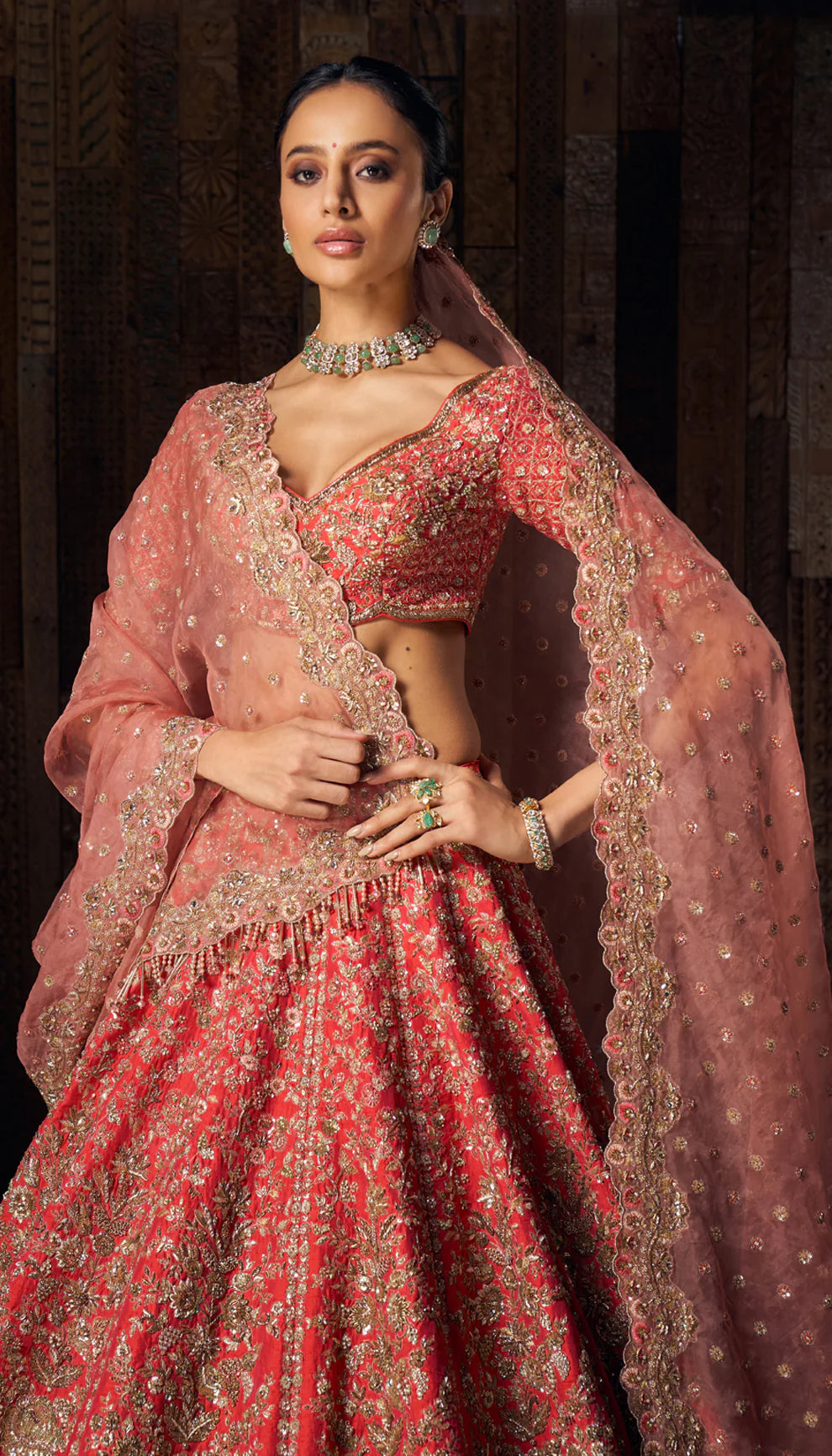 Woman in a red gold embroidered bridal lehenga by designers Shyamal and Bhumika, against a dark wooden backdrop