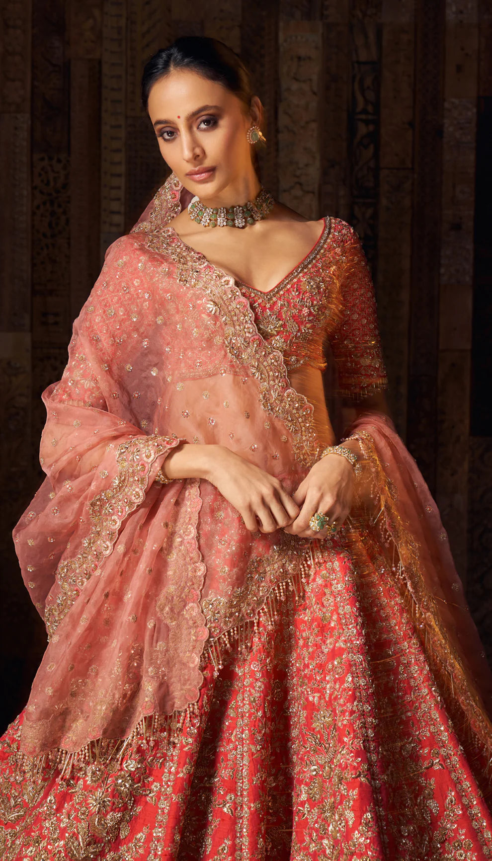 Woman in a red gold embroidered bridal lehenga by designers Shyamal and Bhumika, against a dark wooden backdrop