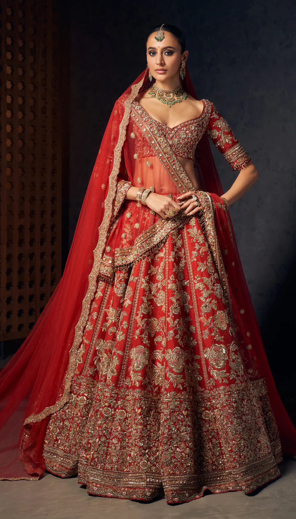 Woman wearing a red and gold embroidered bridal lehenga by designers Shyamal and Bhumika against a dark background