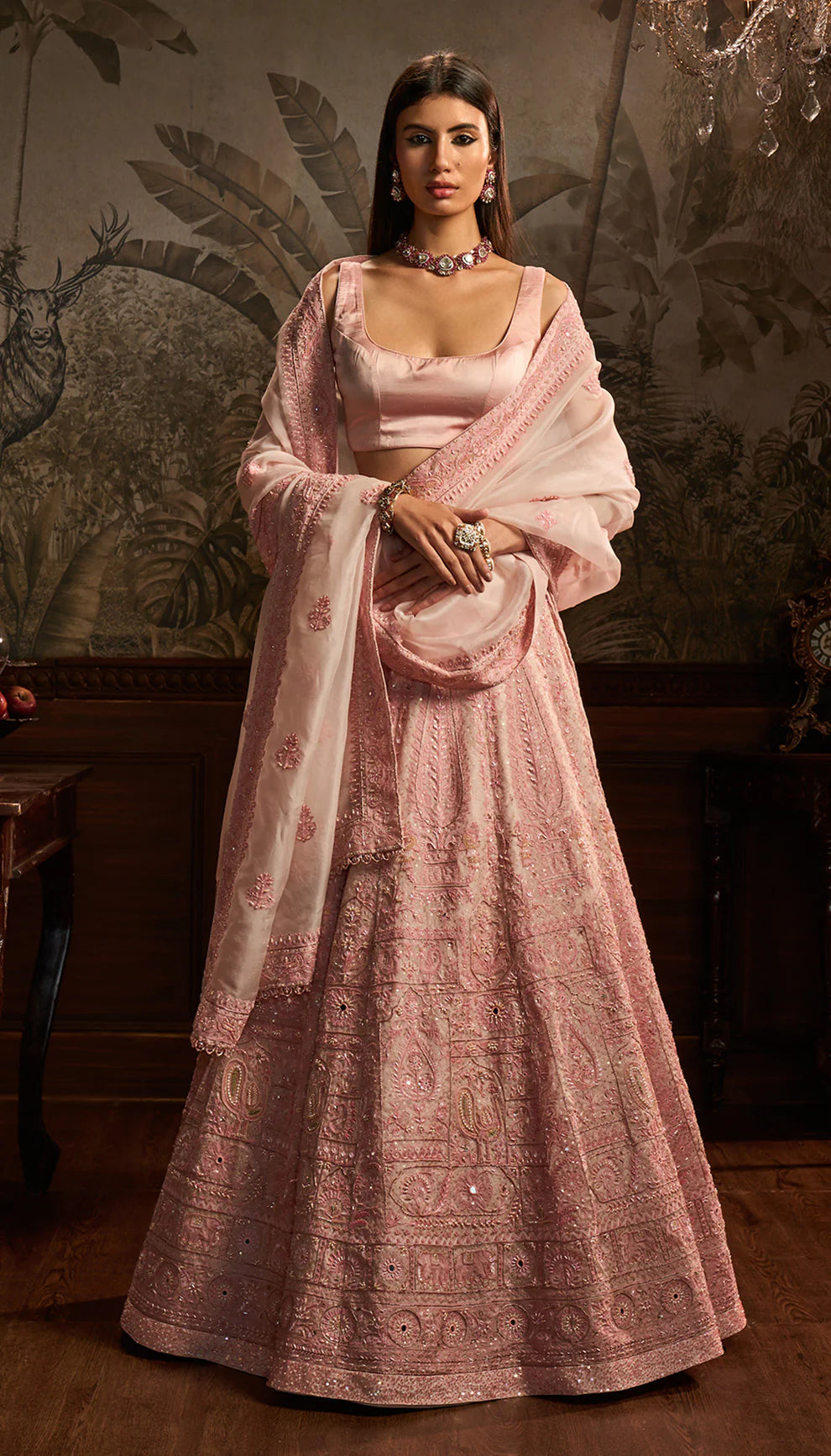 Woman in a traditional pink embroidered lehenga by designers Shyamal and Bhumika with a matching dupatta against a decorative background