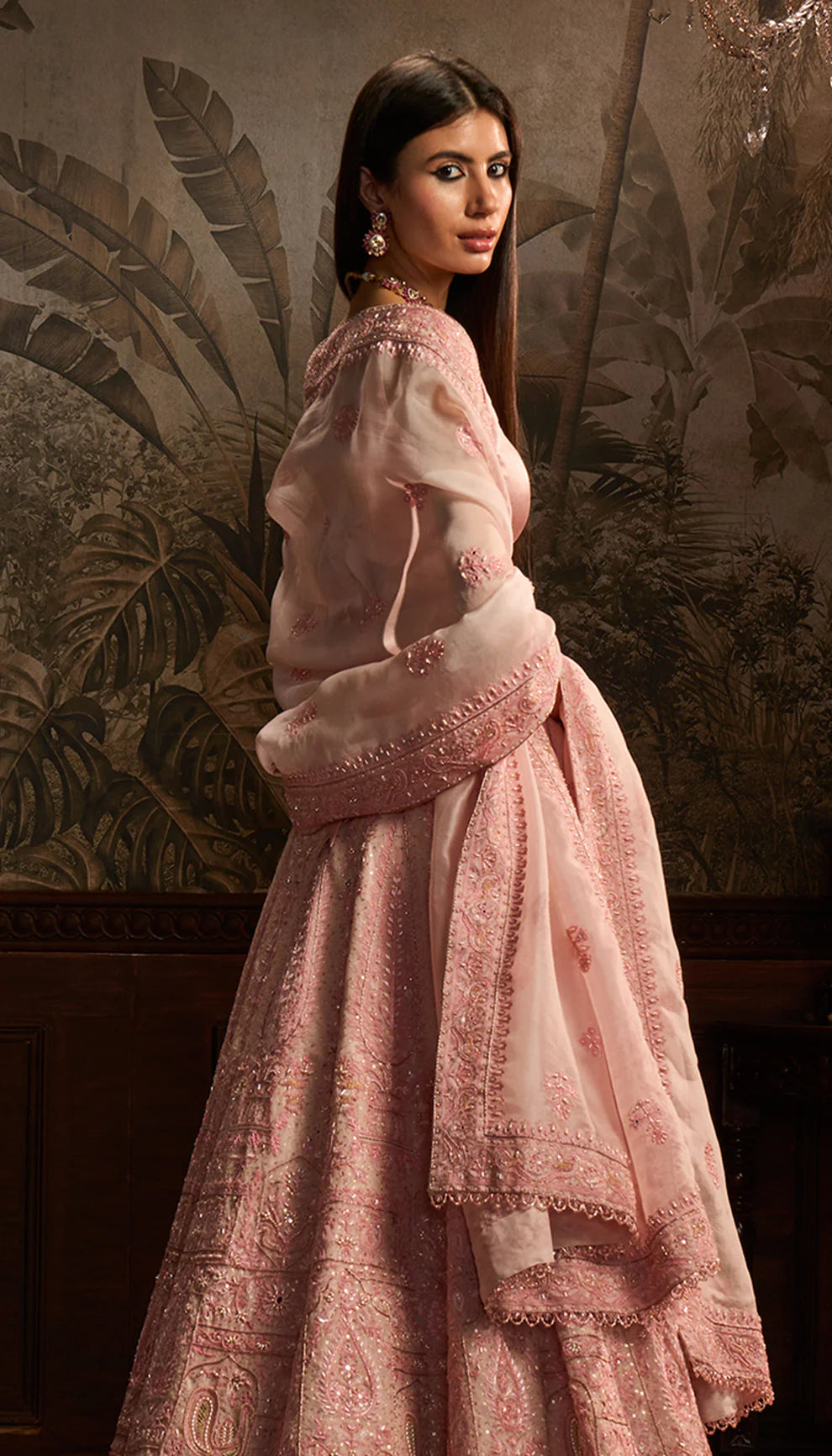 Woman in a traditional pink embroidered lehenga by designers Shyamal and Bhumika with a matching dupatta against a decorative background
