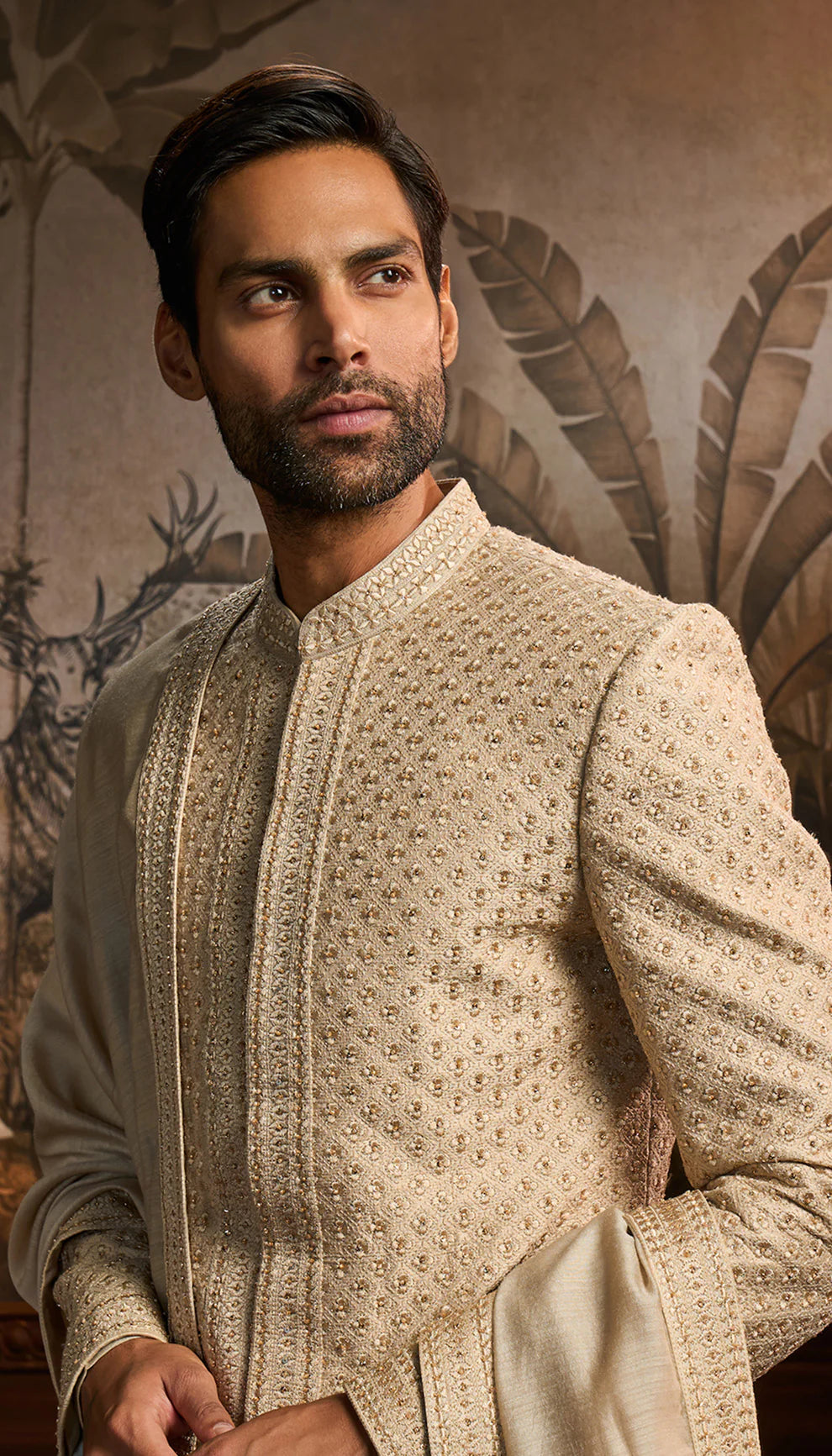 Man wearing a Shyamal and Bhumika ivory sherwani with white pants in an ornate room.