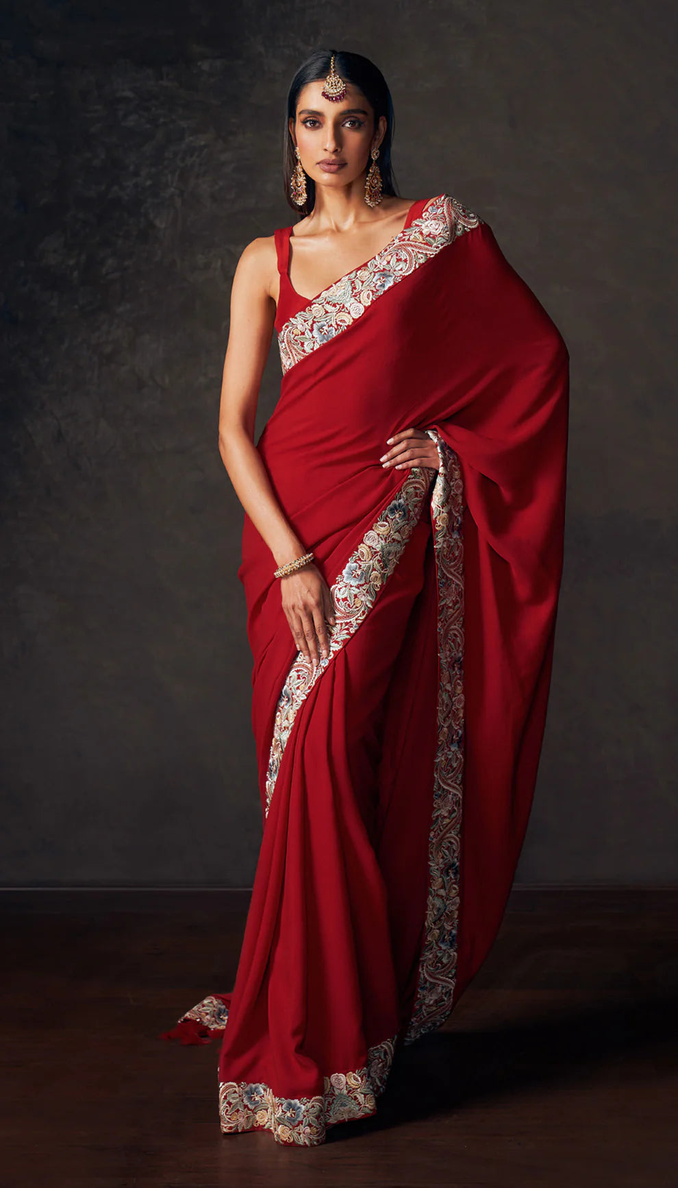 Woman wearing a red saree with embroidered border by designers Shyamal and Bhumika against a dark background