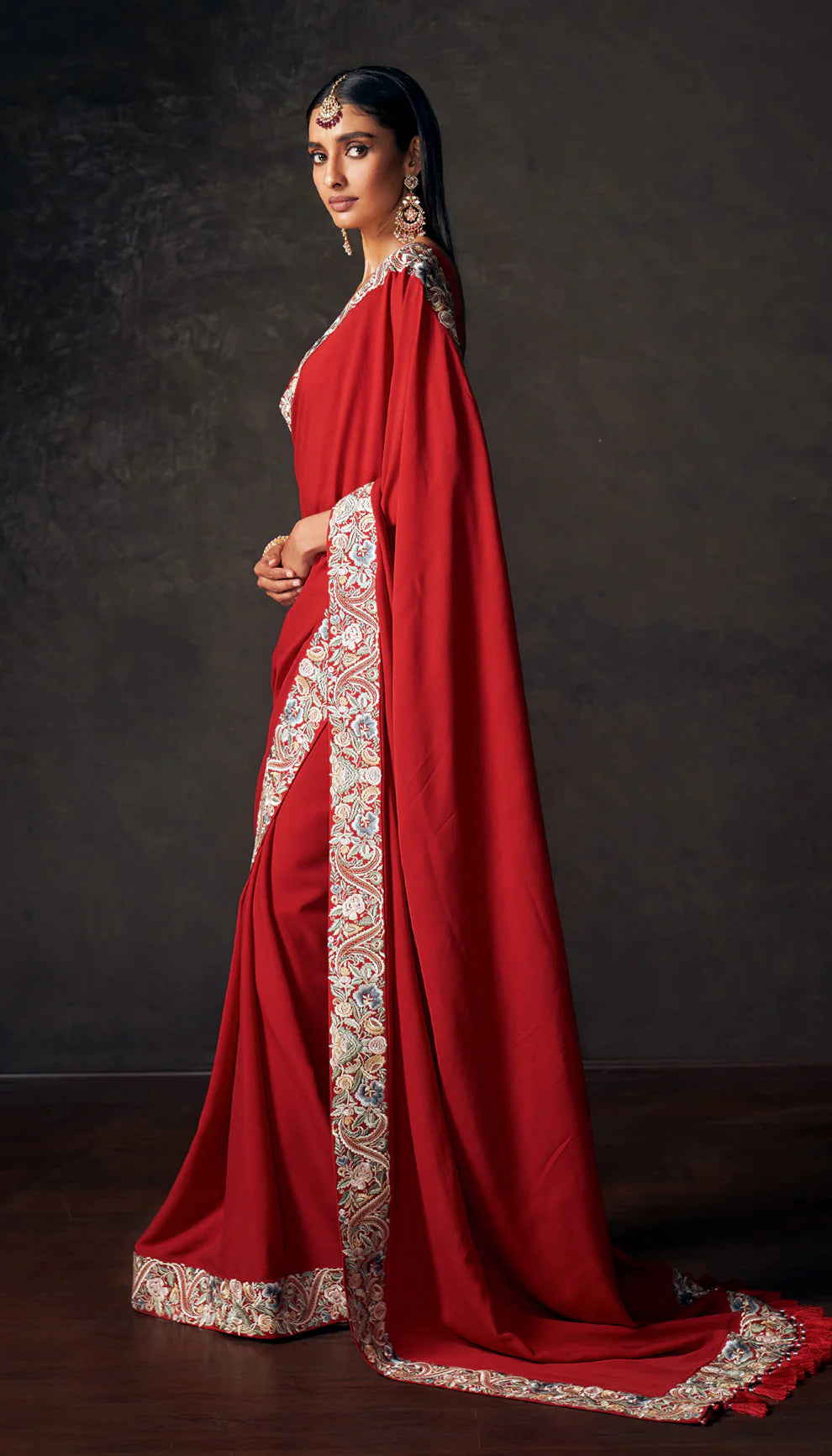 Woman wearing a red saree with embroidered border by designers Shyamal and Bhumika against a dark background