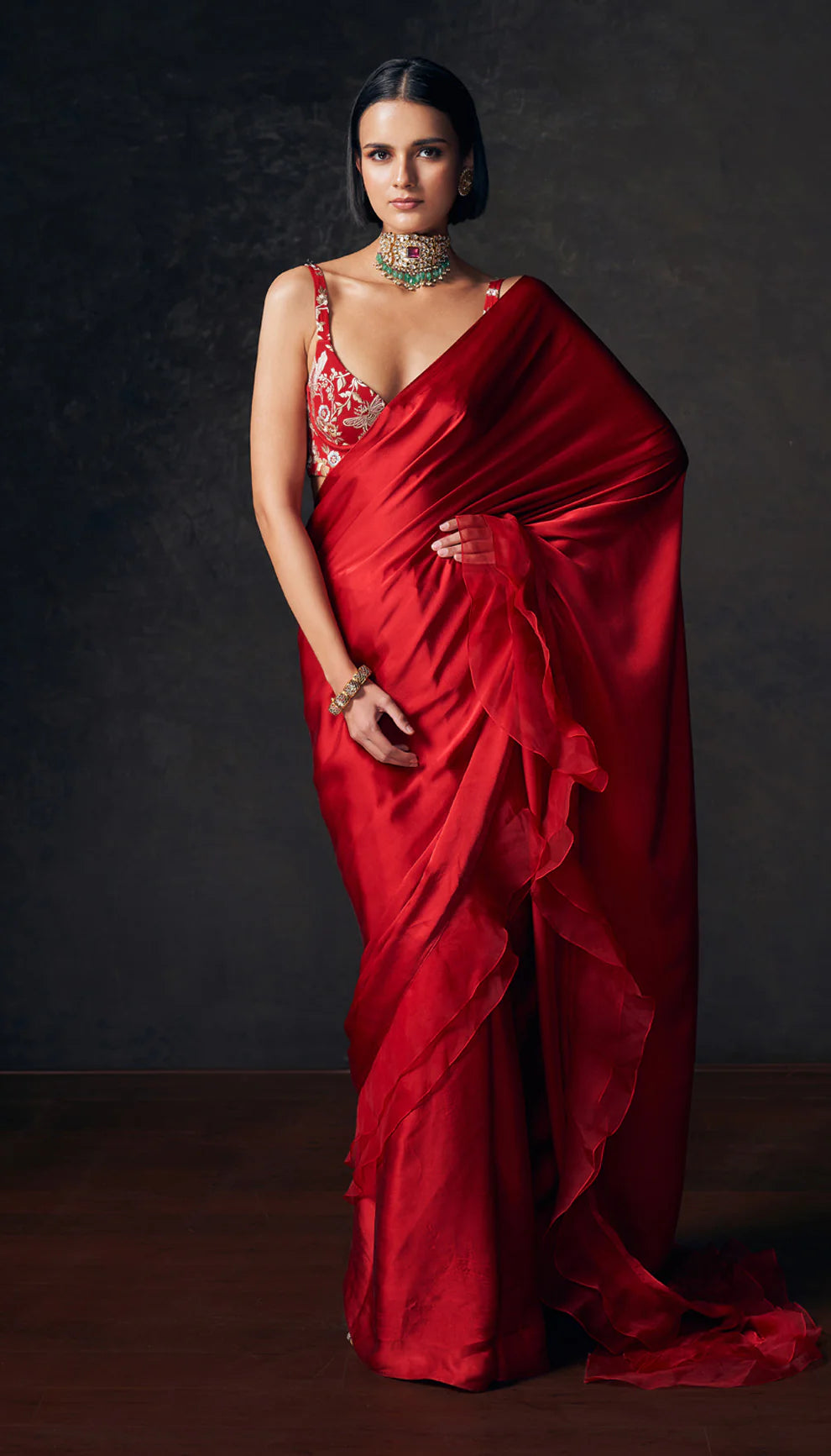 Woman in a red saree with intricate designs by designers Shyamal and Bhumika against a dark background