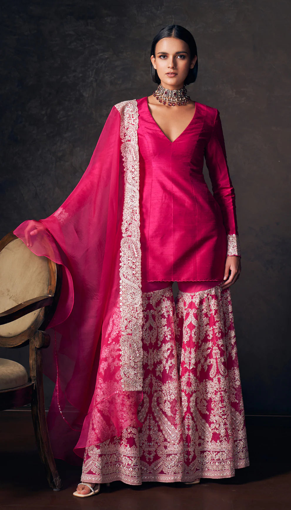 Woman wearing a pink traditional sharara set with a patterned dupatta by designers Shyamal and Bhumika against a dark background