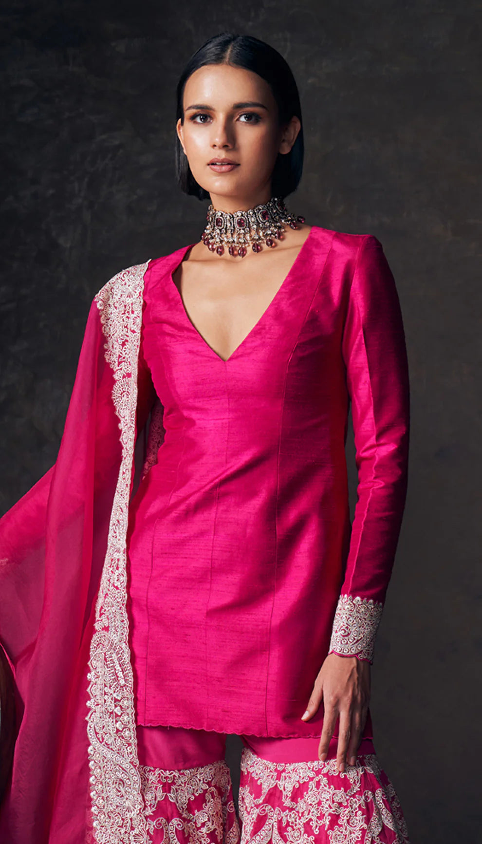 Woman wearing a pink traditional sharara set with a patterned dupatta by designers Shyamal and Bhumika against a dark background