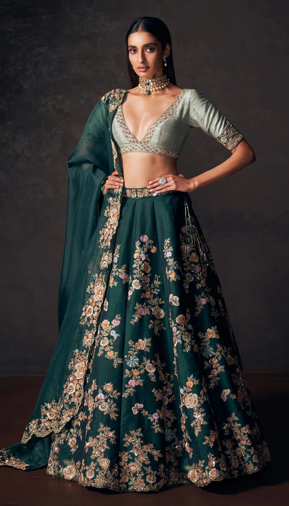Woman wearing a traditional forest green lehenga with a floral design by designers Shyamal and Bhumika on a dark background