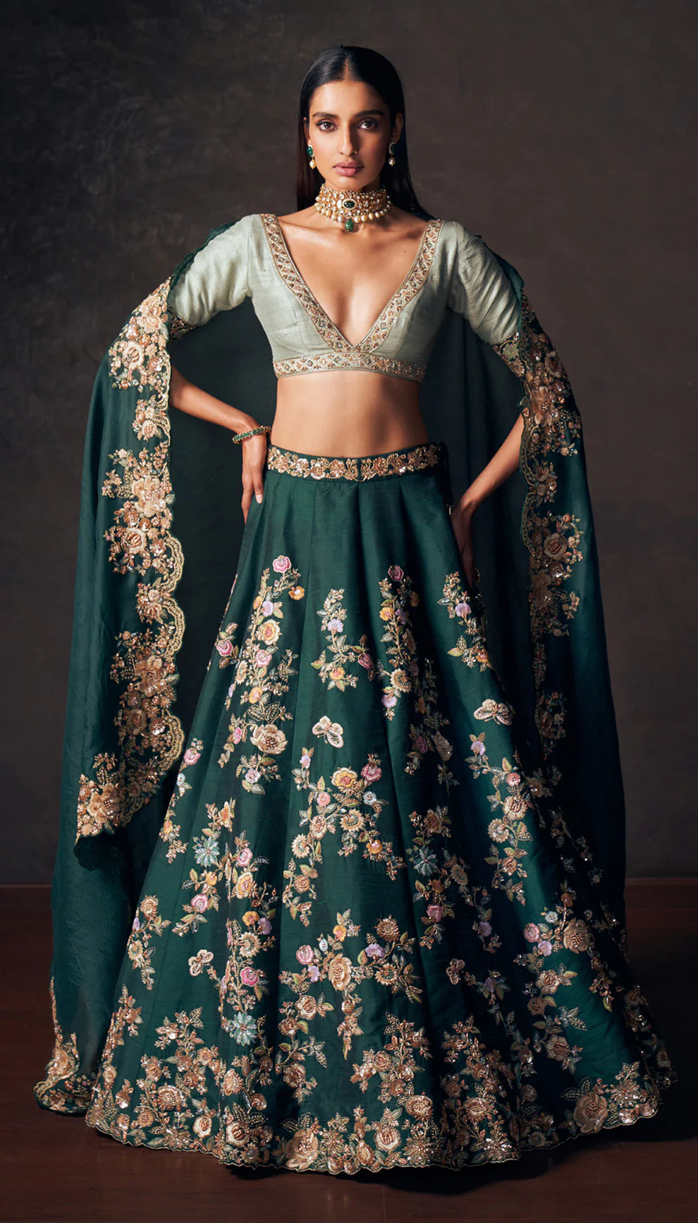 Woman wearing a traditional forest green lehenga with a floral design by designers Shyamal and Bhumika on a dark background