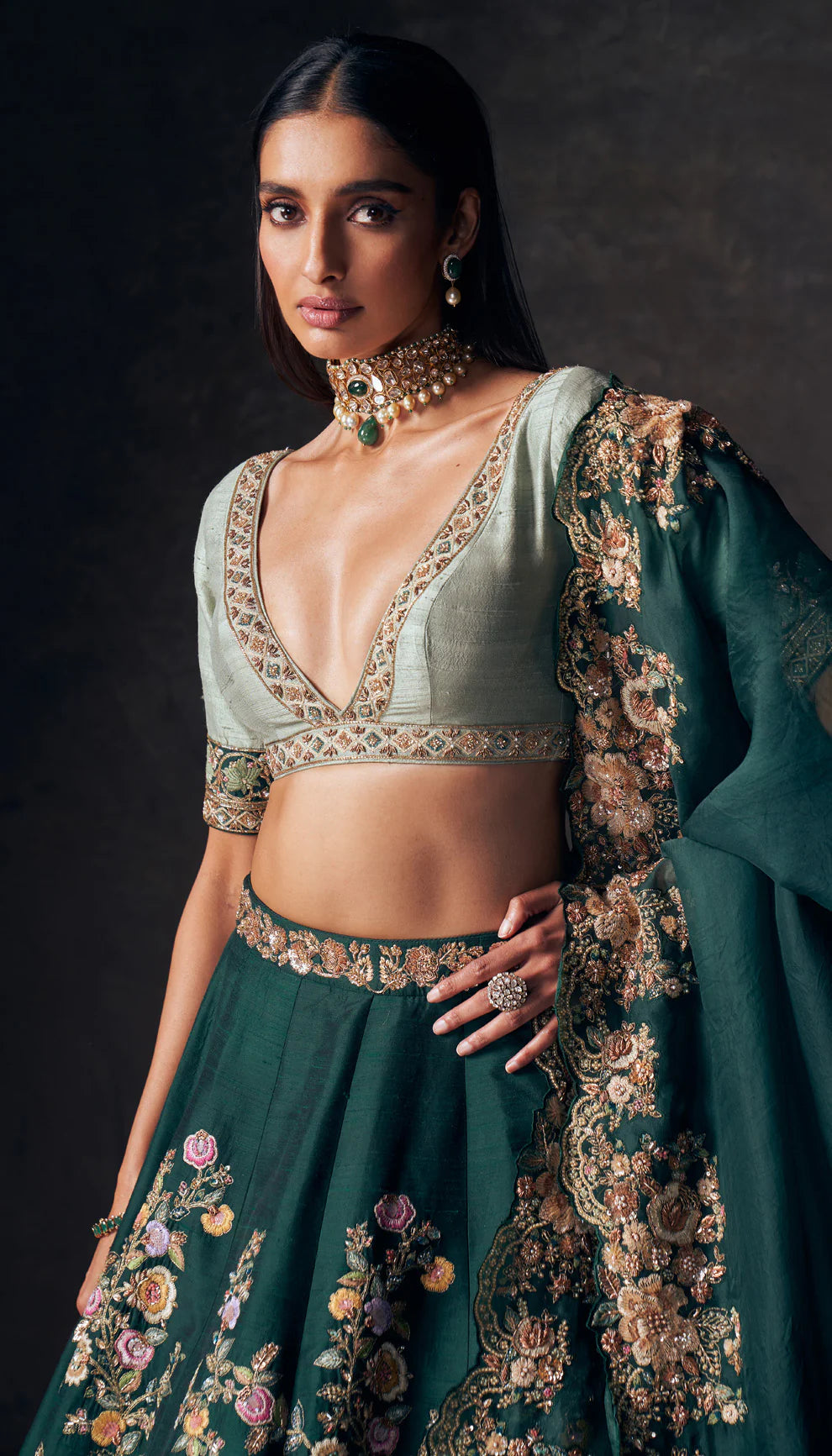 Woman wearing a traditional forest green lehenga with a floral design by designers Shyamal and Bhumika on a dark background