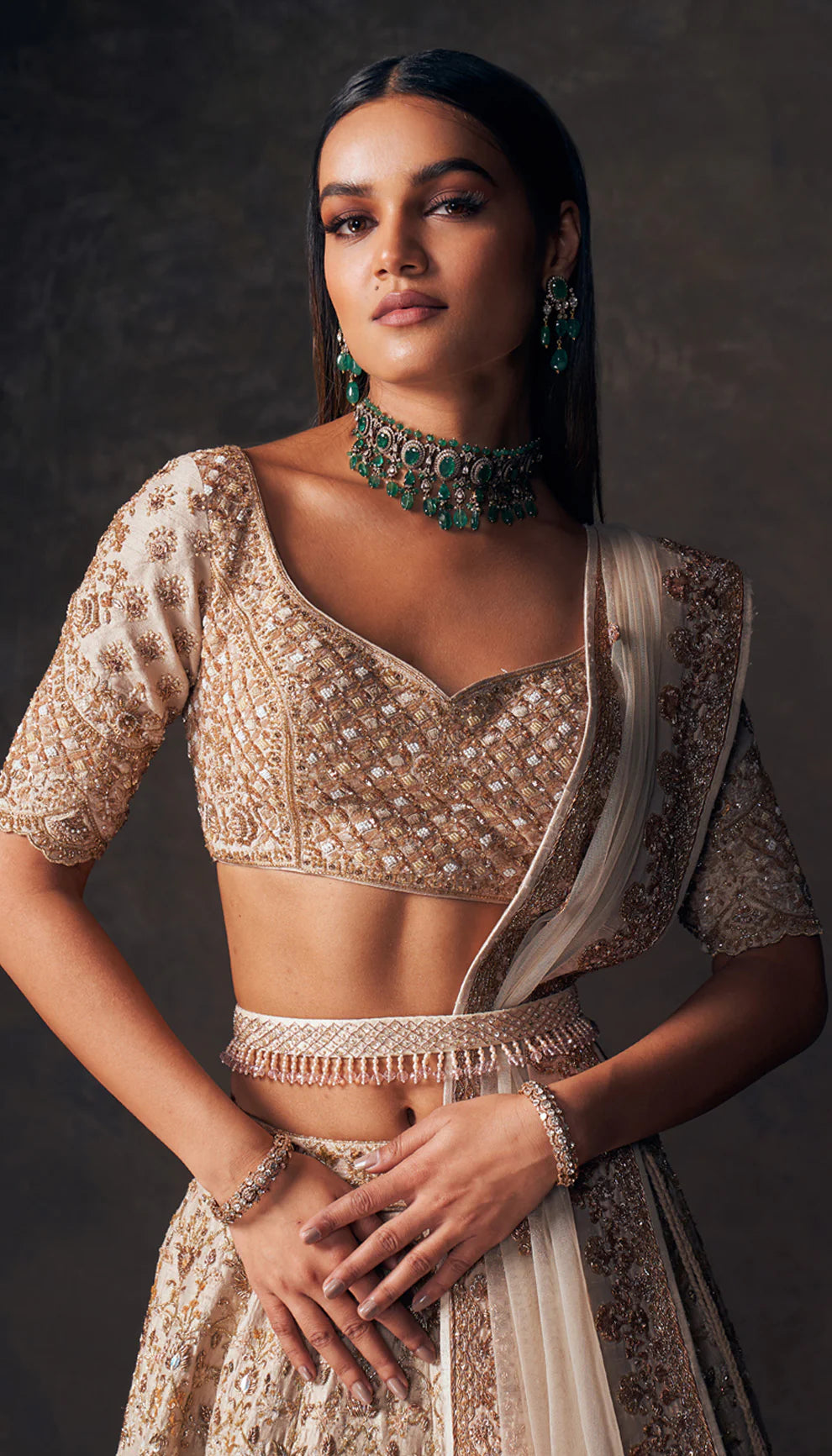 Woman wearing a beige traditional lehenga with intricate patterns by designers Shyamal and Bhumika, on a dark background