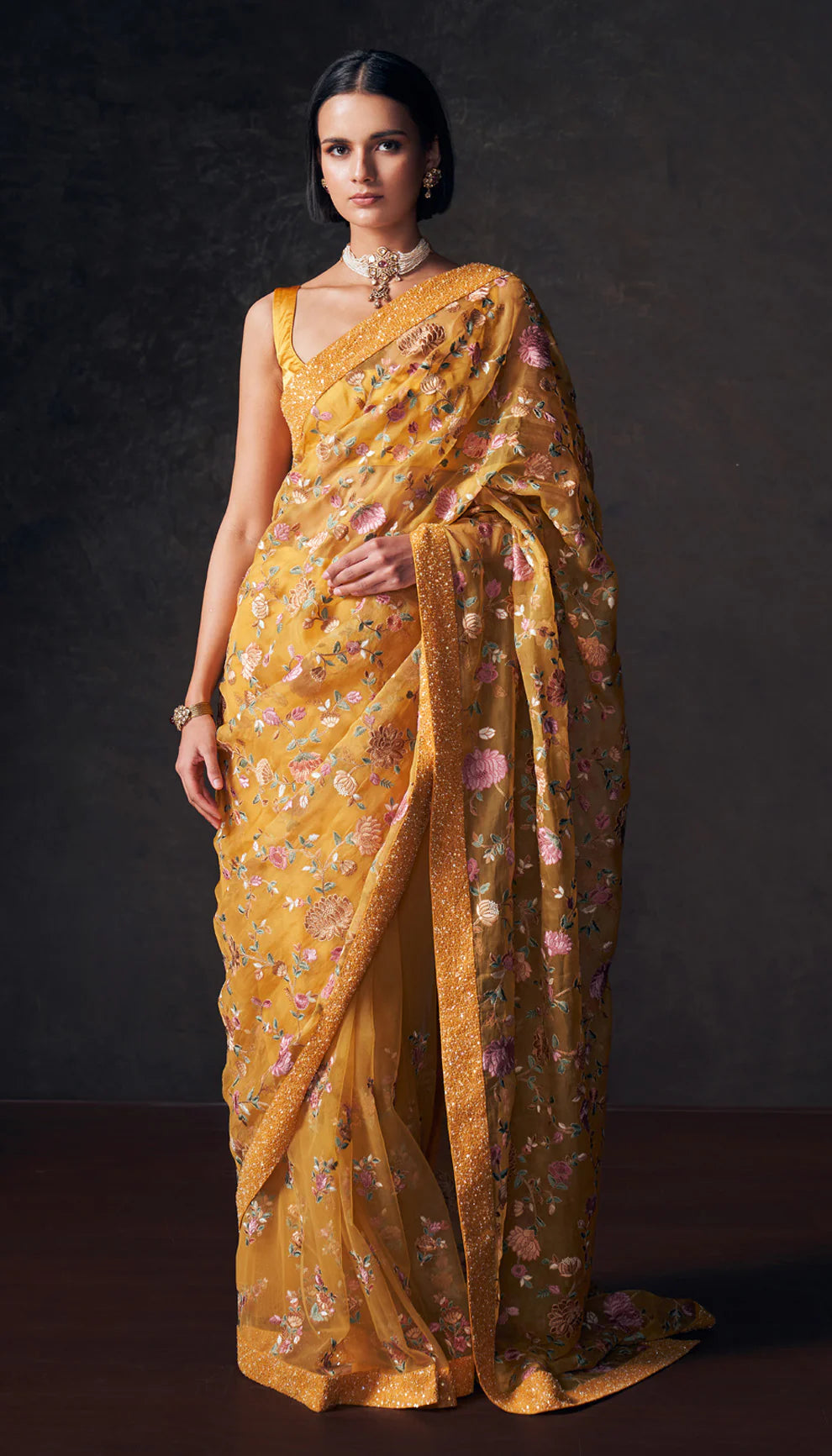 Woman wearing a ochre yellow saree by designers Shyamal and Bhumika with a dark background