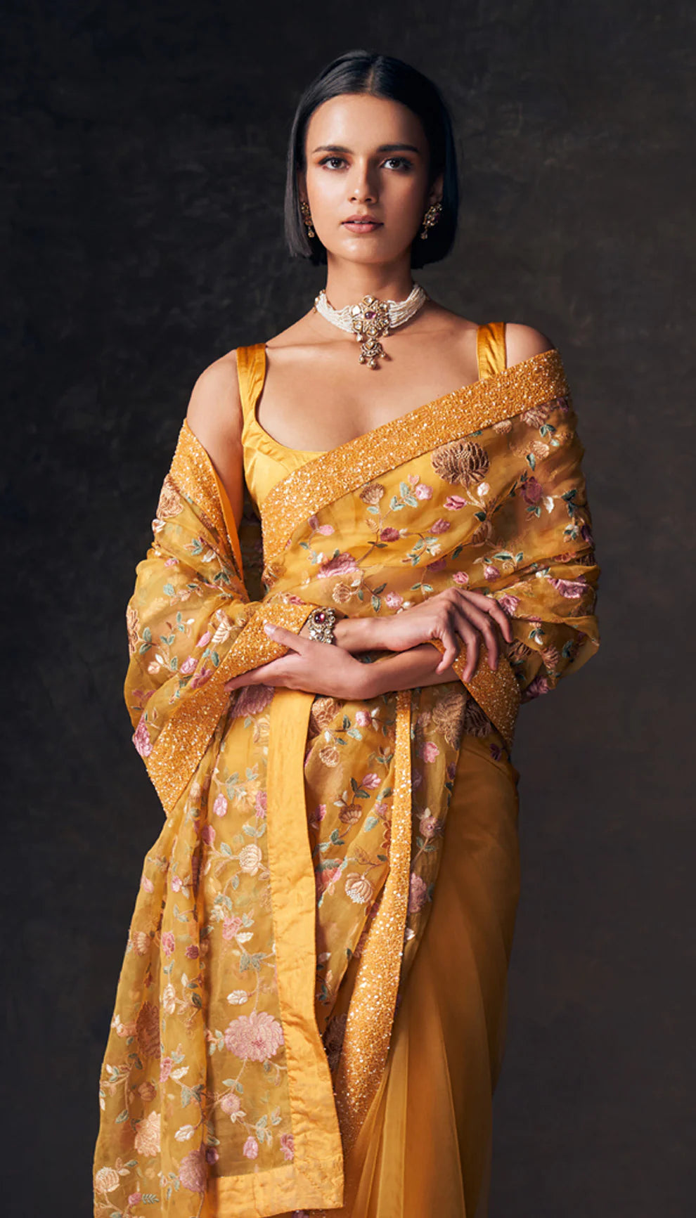 Woman wearing a ochre yellow saree by designers Shyamal and Bhumika with a dark background