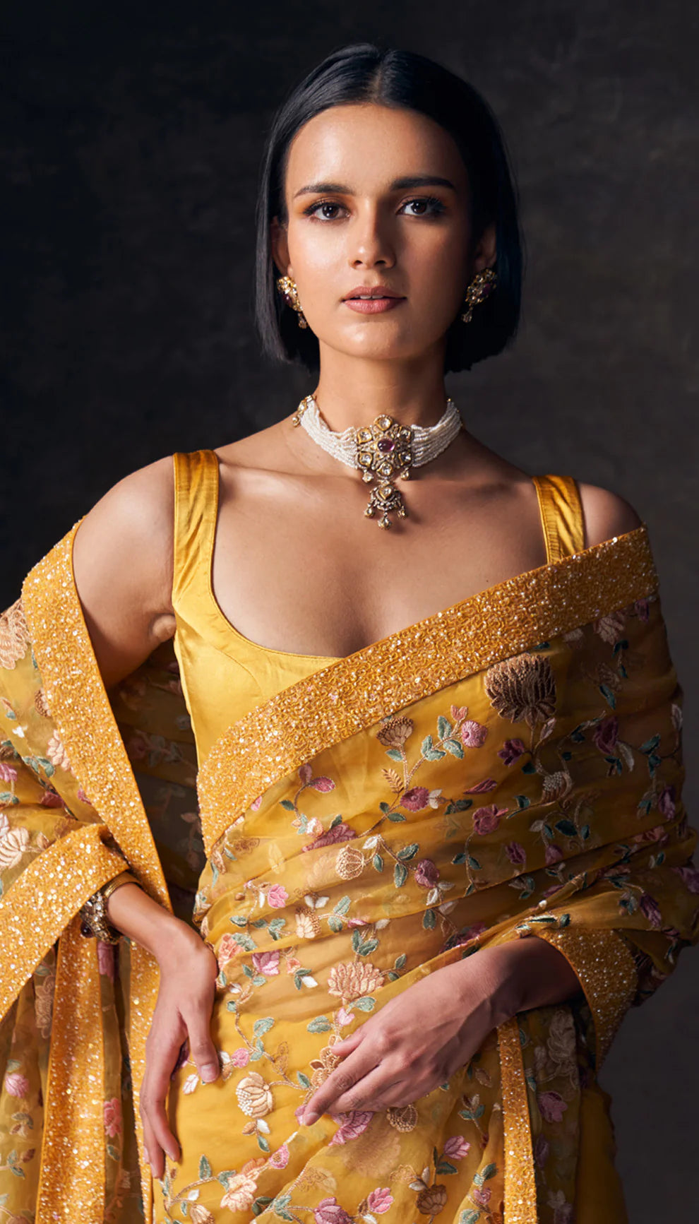 Woman wearing a ochre yellow saree by designers Shyamal and Bhumika with a dark background