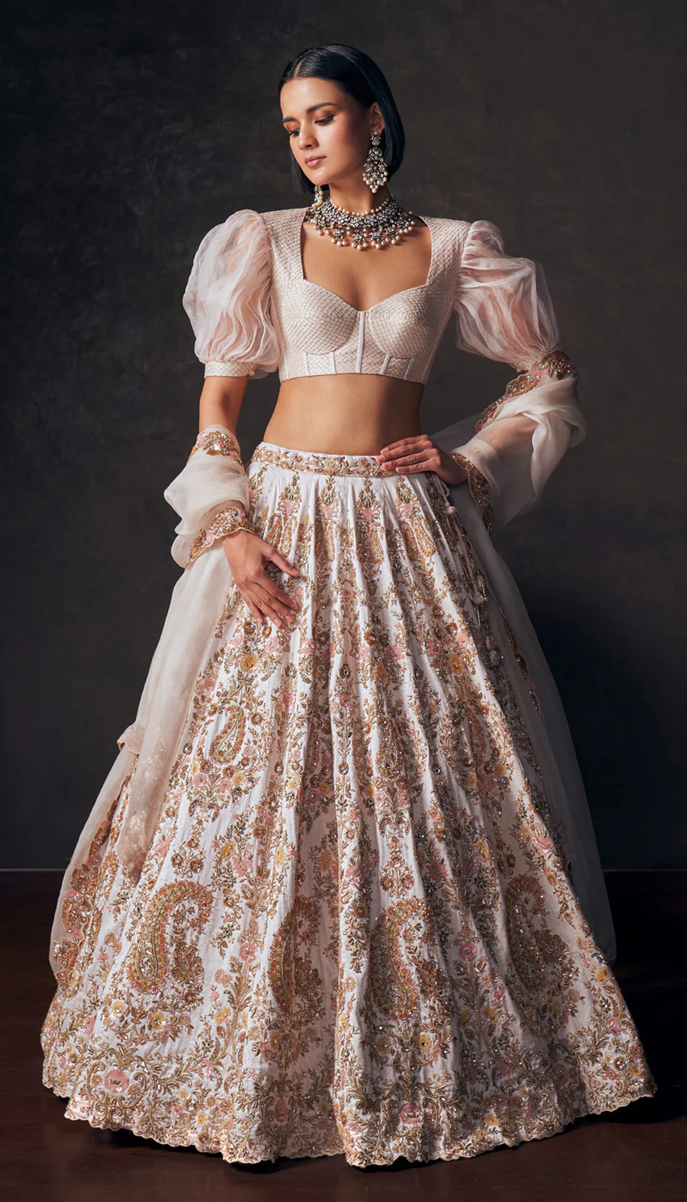 Woman wearing an ivory traditional lehenga with a white blouse and patterned skirt by designers Shyamal and Bhumika against a dark background