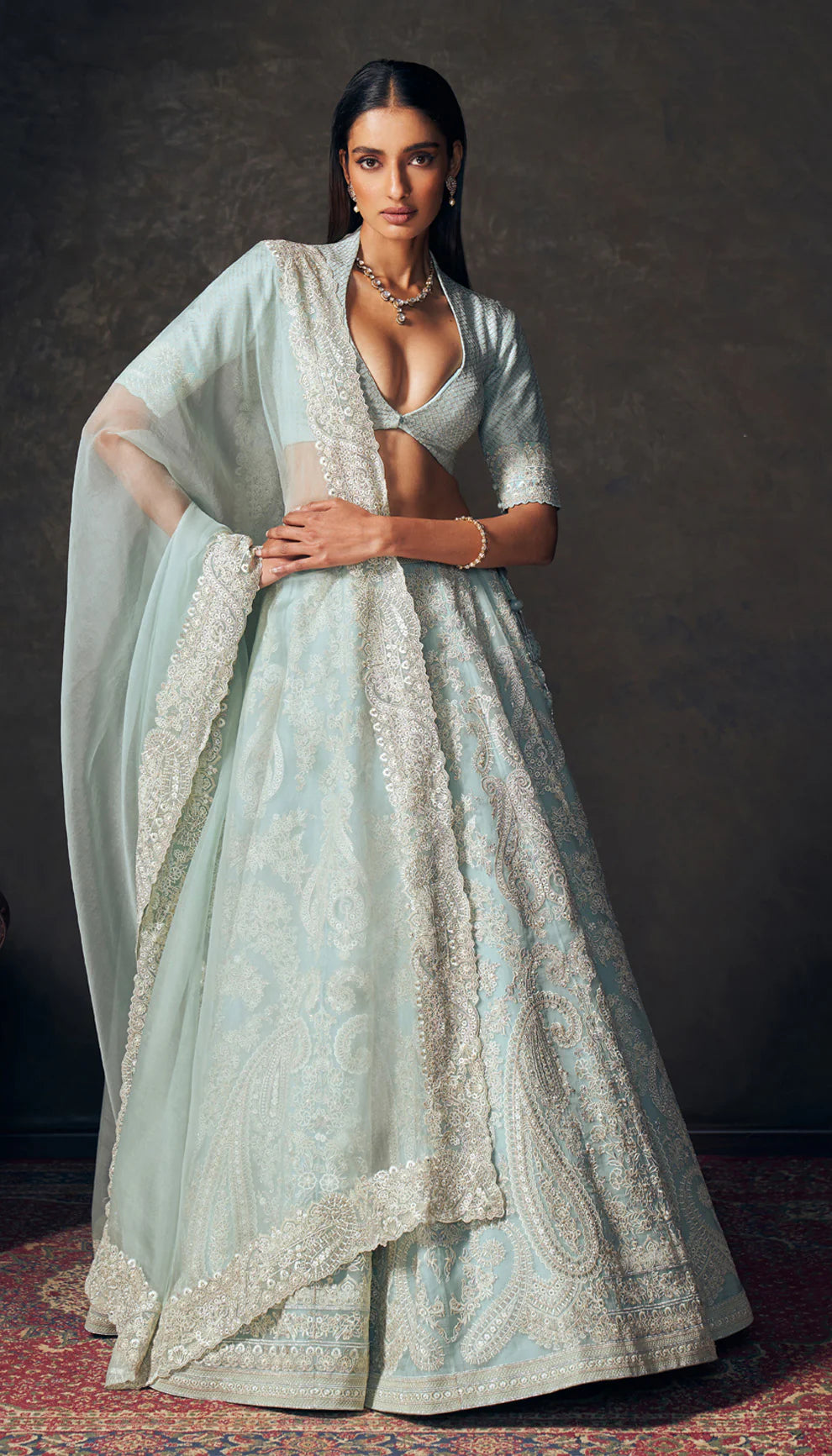 Woman in a light blue traditional lehenga by designers Shyamal and Bhumika with a dark background
