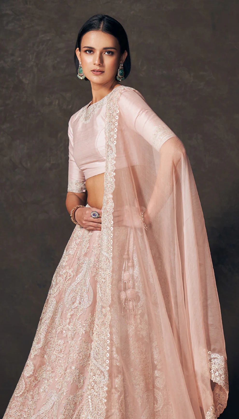 Woman wearing a traditional pink lehenga with a matching blouse by designers Shyamal and Bhumika against a dark background