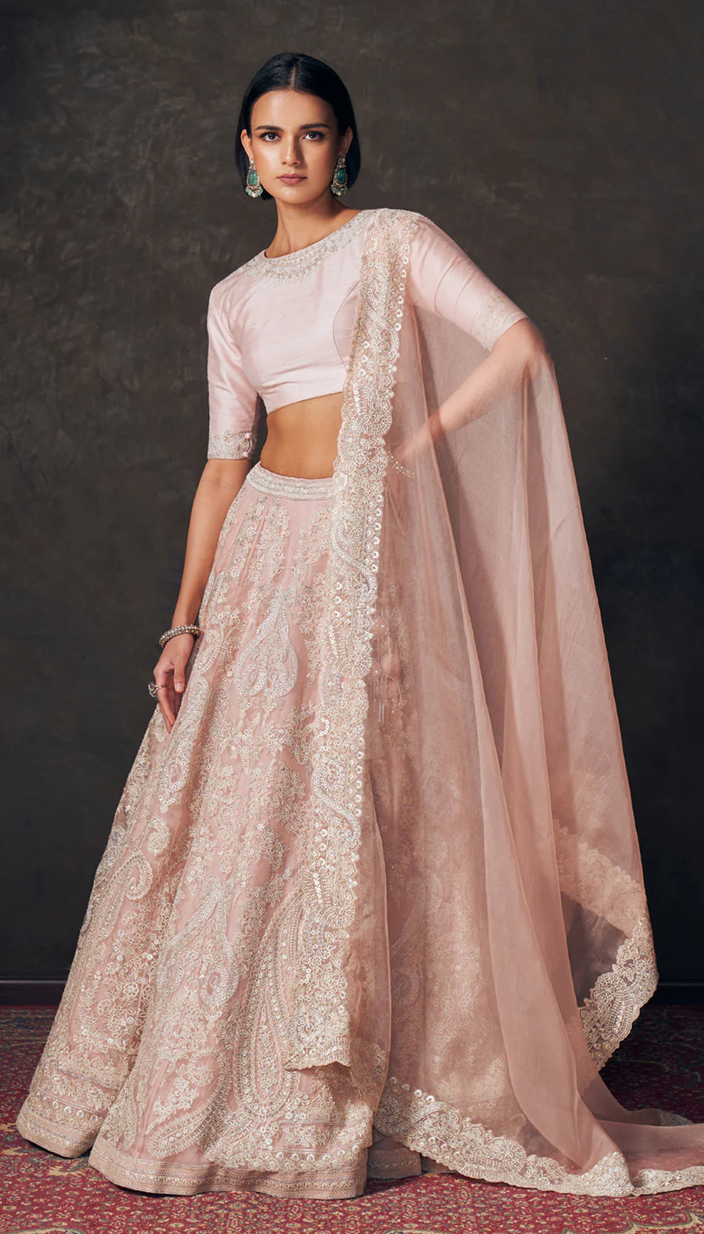 Woman wearing a traditional pink lehenga with a matching blouse by designers Shyamal and Bhumika against a dark background