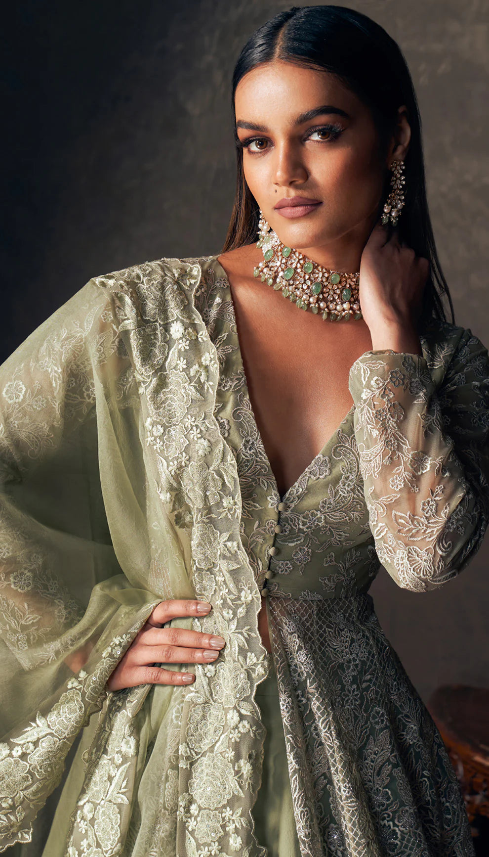 Woman wearing an olive green embroidered jacket by designers Shyamal and Bhumika with a dark background