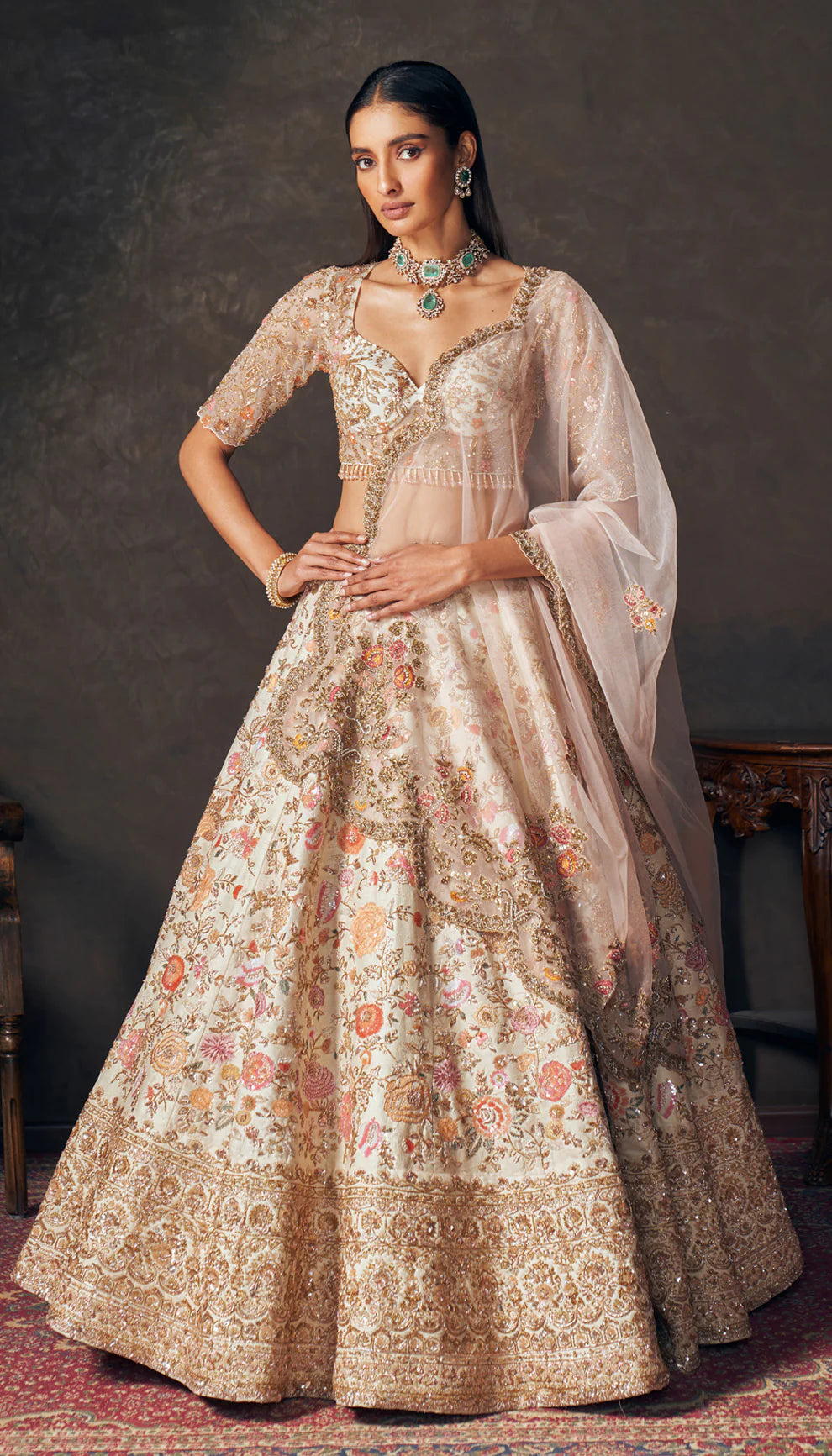 Woman wearing an ivory traditional embroidered lehenga by designers Shyamal and Bhumika with a dark background