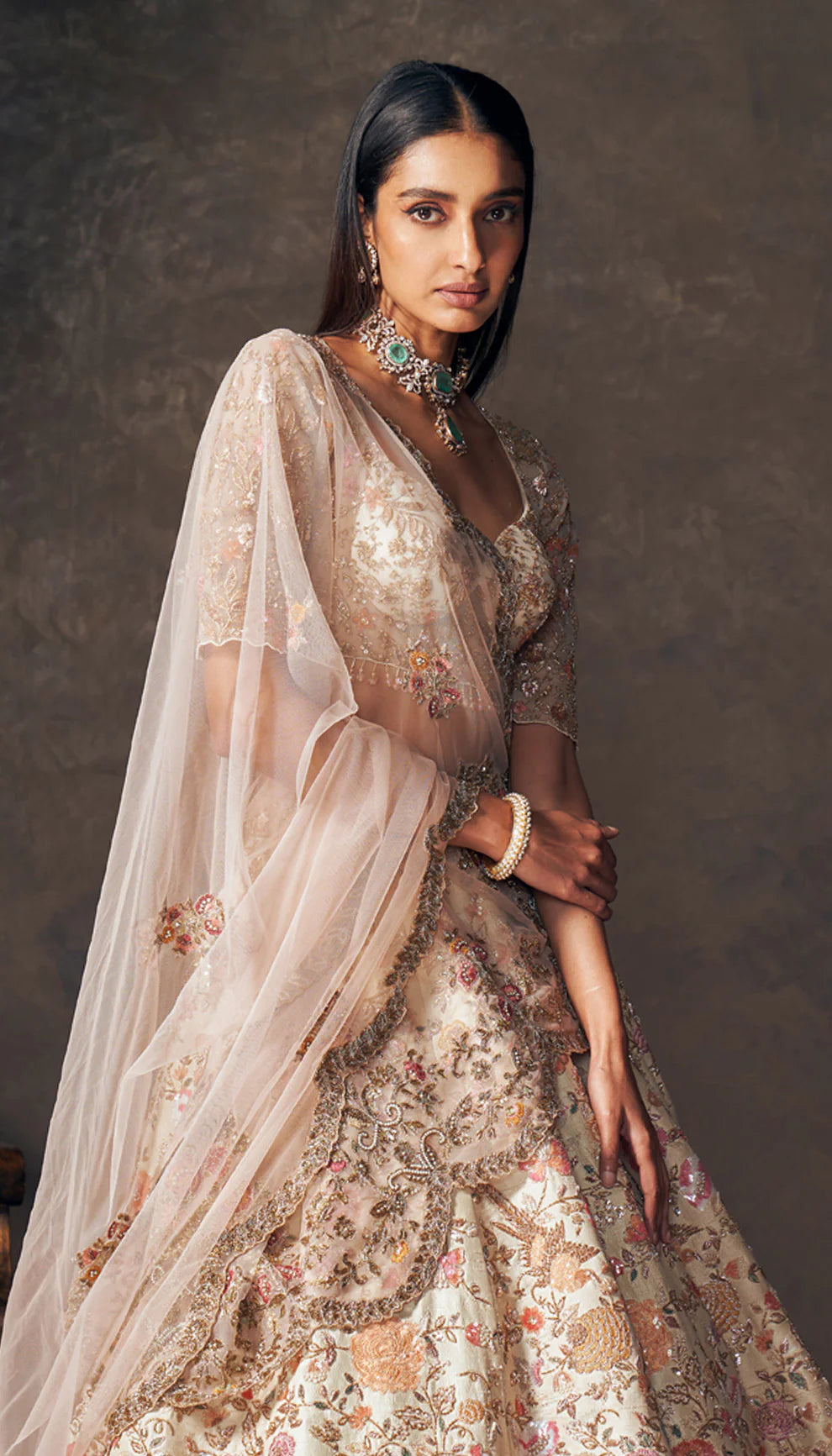 Woman wearing an ivory traditional embroidered lehenga by designers Shyamal and Bhumika with a dark background