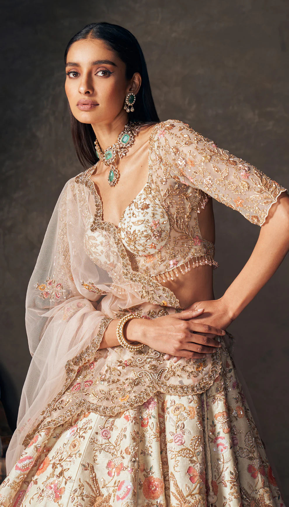 Woman wearing an ivory traditional embroidered lehenga by designers Shyamal and Bhumika with a dark background