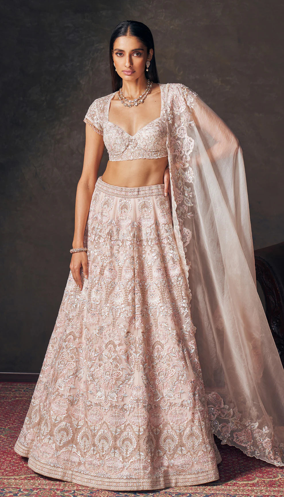 Woman wearing a light pink traditional embroidered lehenga by designers Shyamal and Bhumika with a dark background