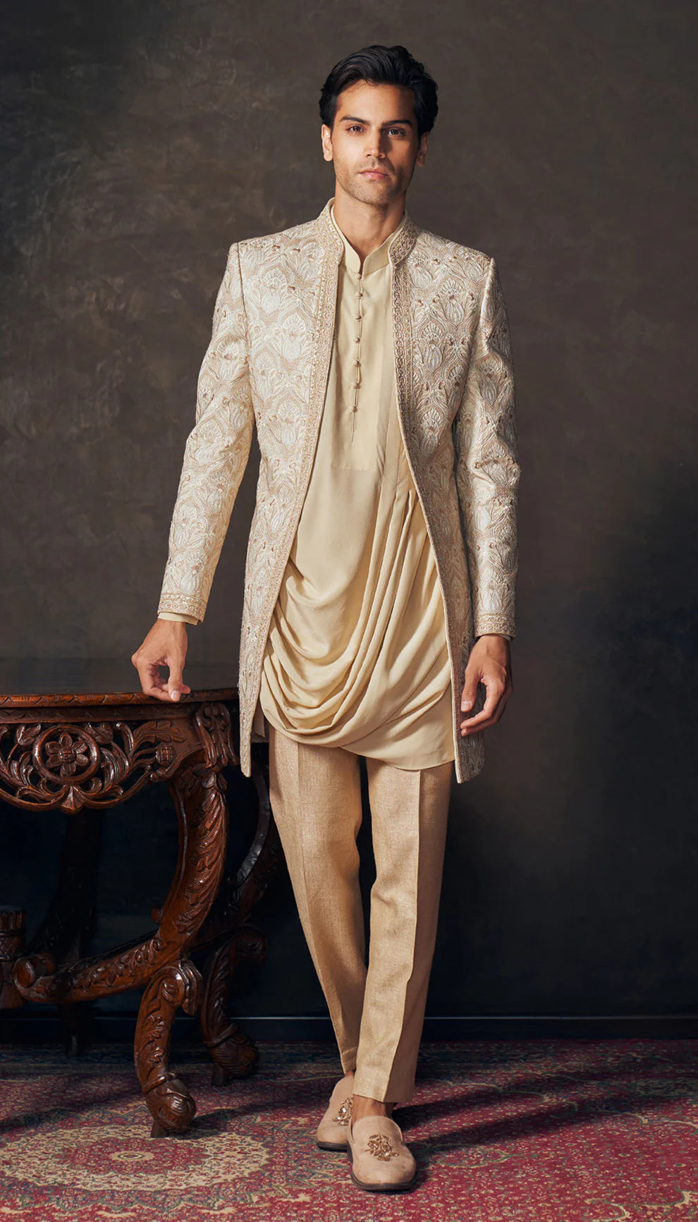 Man wearing a traditional beige embroidered jacket by designers Shyamal and Bhumika against a dark background