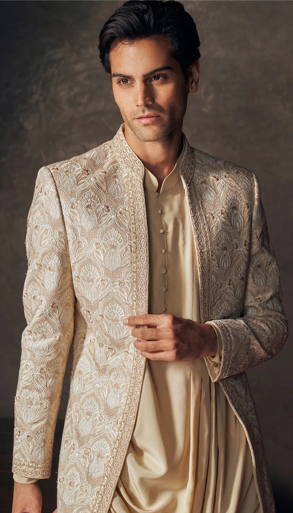 Man wearing a traditional beige embroidered jacket by designers Shyamal and Bhumika against a dark background