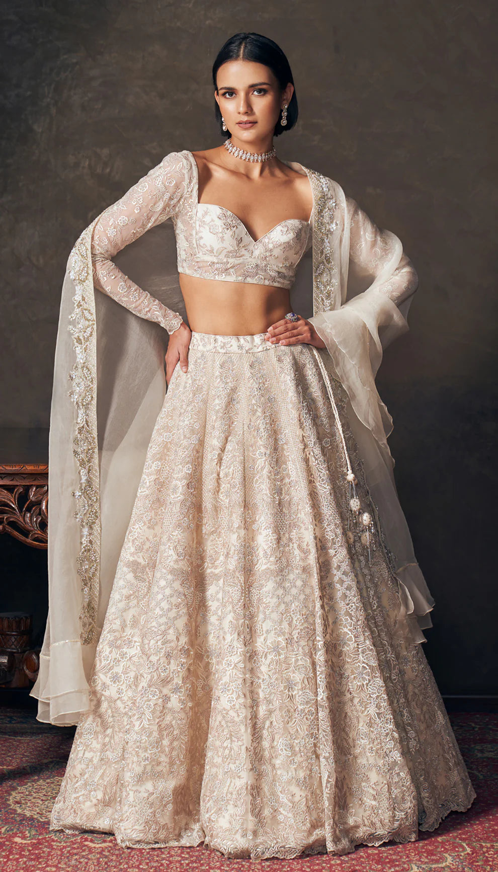 Woman wearing an ivory traditional embroidered lehenga by designers Shyamal and Bhumika with a dark background